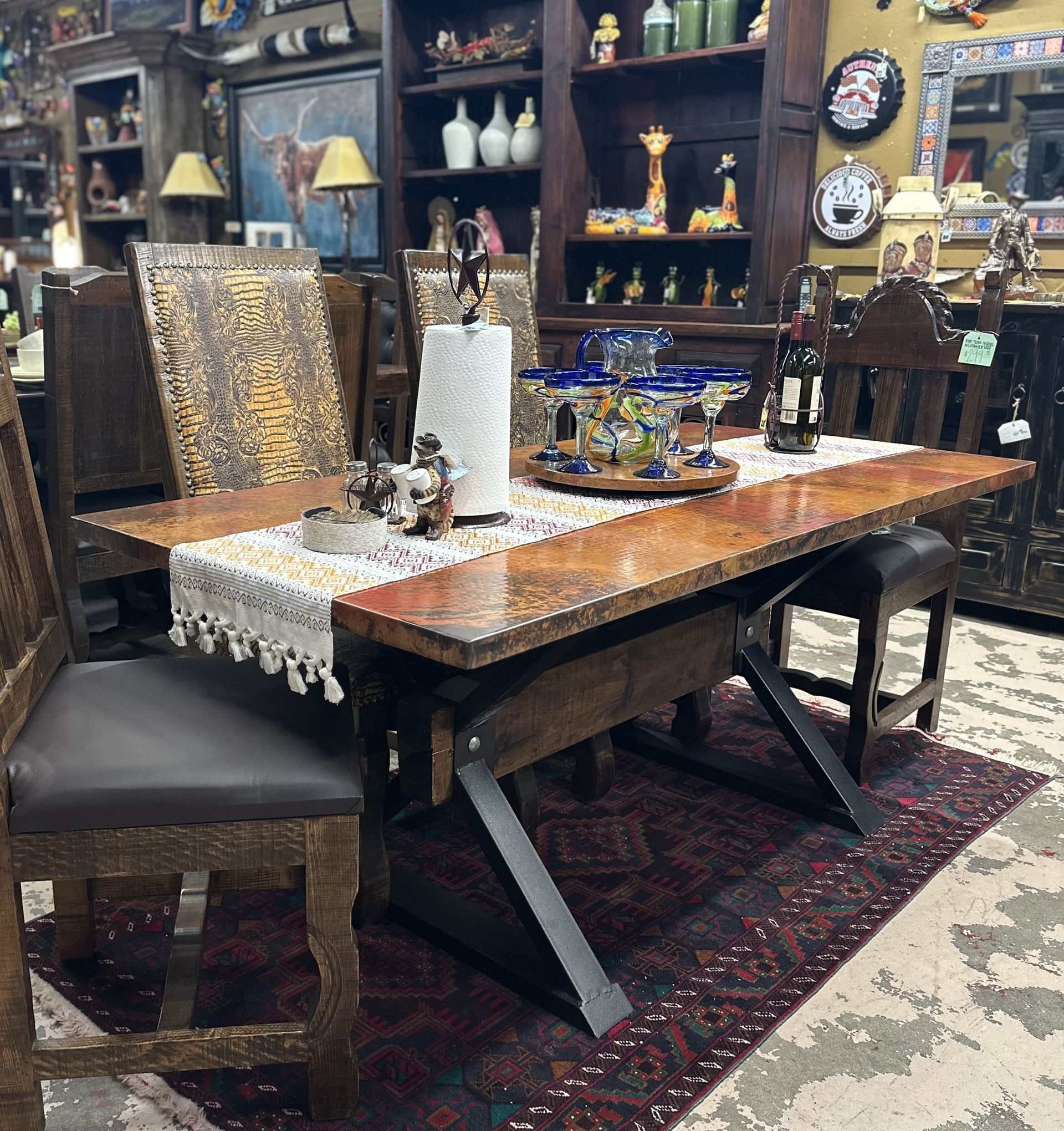 A dining table with chairs, set with place settings.  The room has a rustic, southwestern aesthetic, with display shelves in the background.