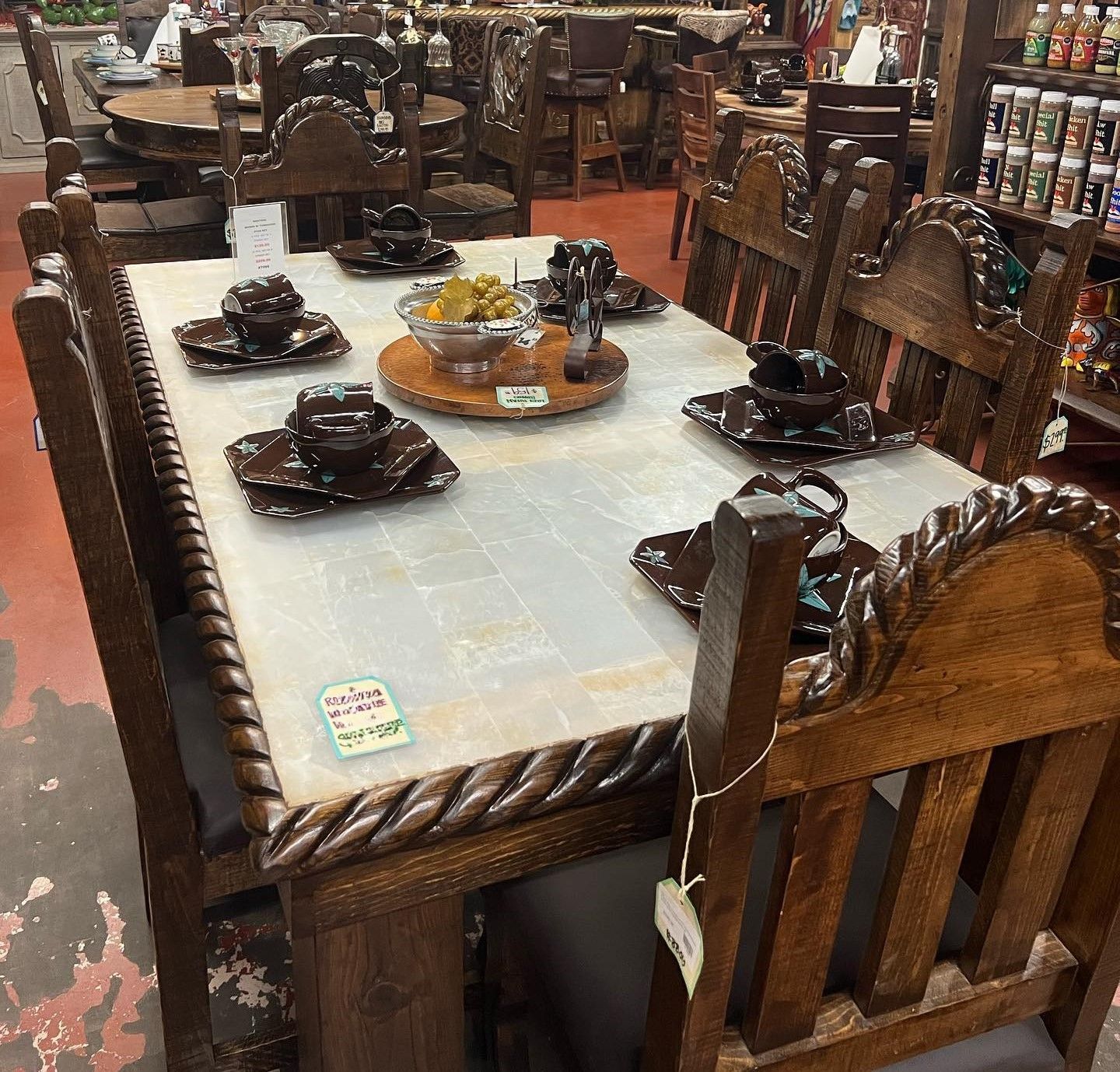 A rustic wooden dining table with six matching chairs, each set with dishes. Brown tones dominate the scene.