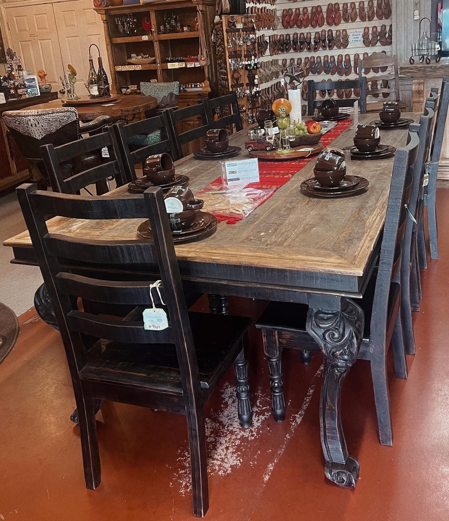 A large, rustic wooden dining table set for a meal with black chairs. A red runner sits in the center.
