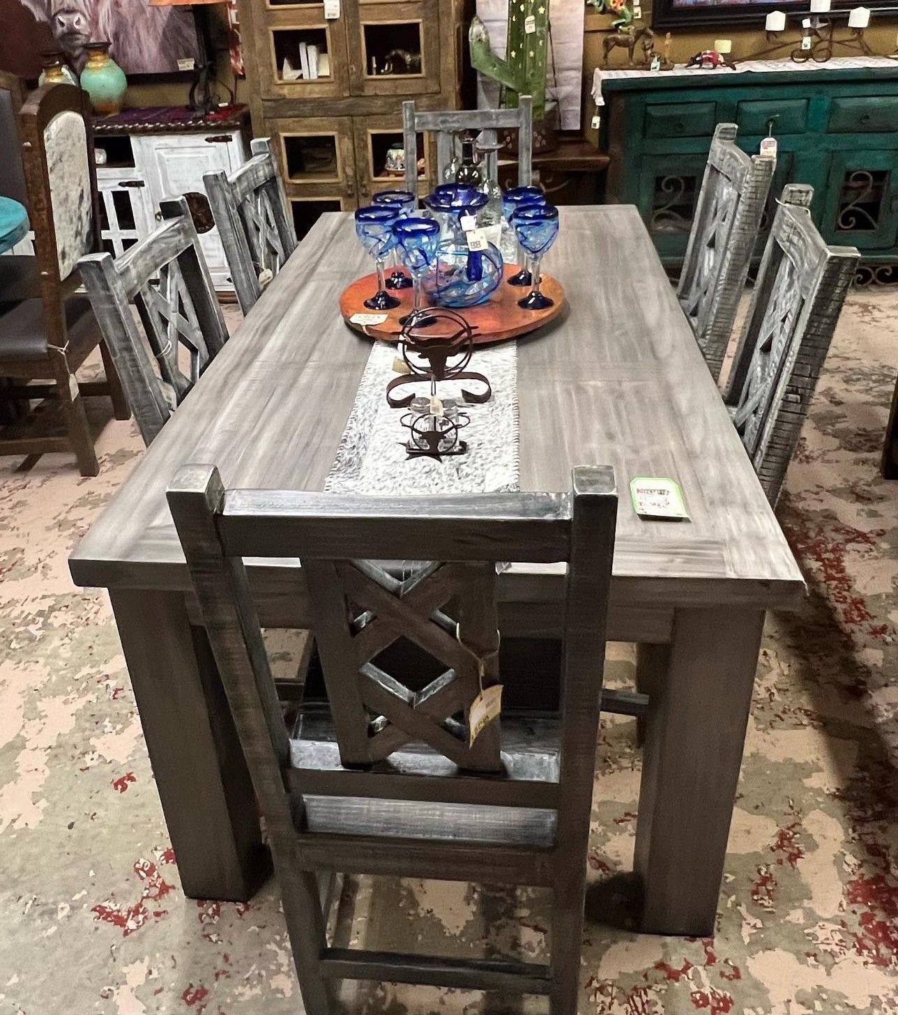 Rustic wooden dining table with eight matching chairs. The table is set with glassware, a decorative runner, and other embellishments.