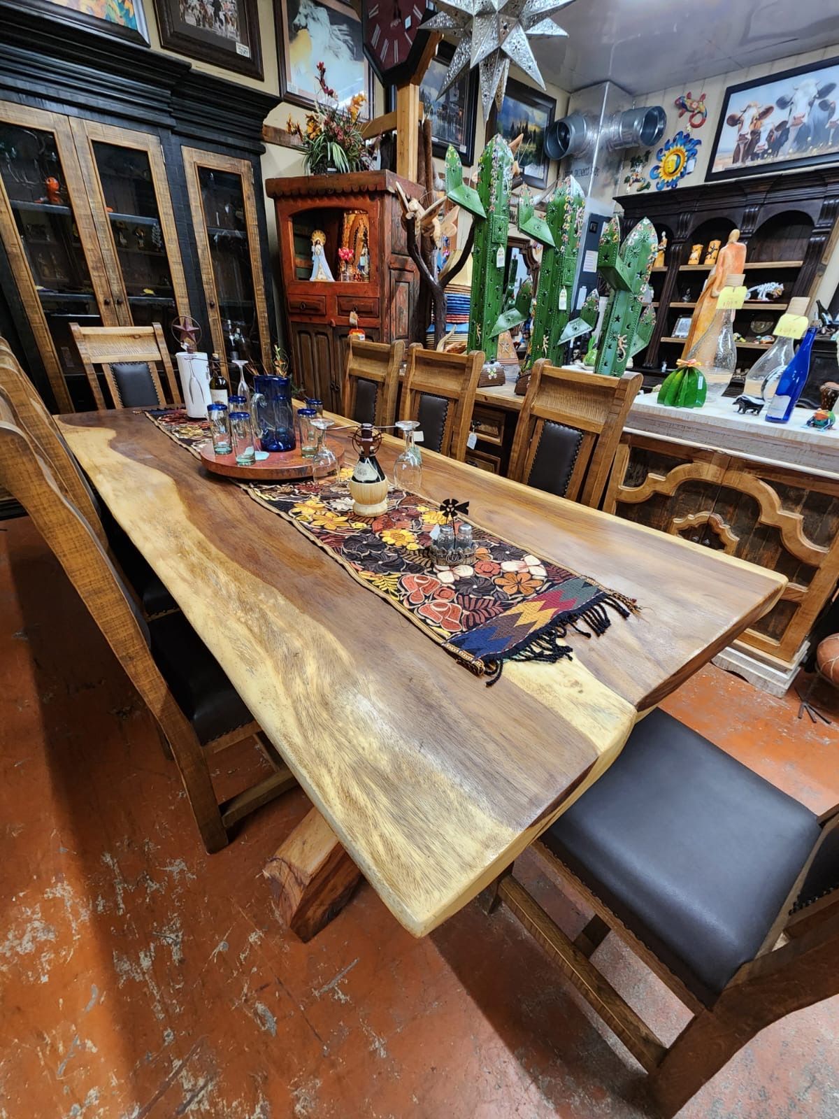 Wooden dining table with chairs in a furniture store; decorated with a runner and centerpieces, and the chairs are brown.
