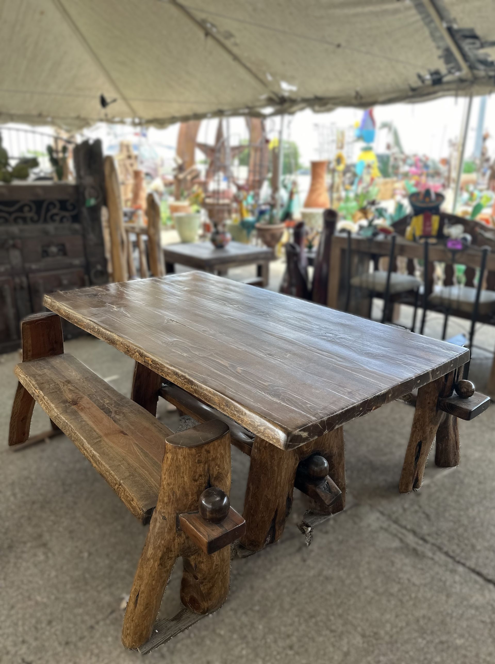 Wooden rustic picnic table and bench set in an outdoor market setting, with other decor items visible in the background.