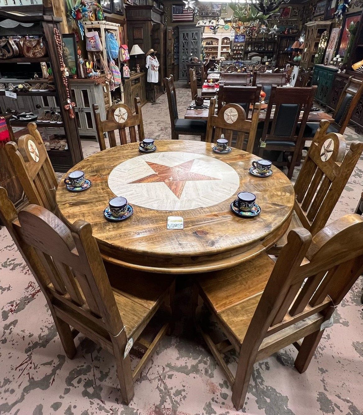 A rustic round dining table with eight chairs, a large star design in the center. The chairs and table are wood, in a store setting.