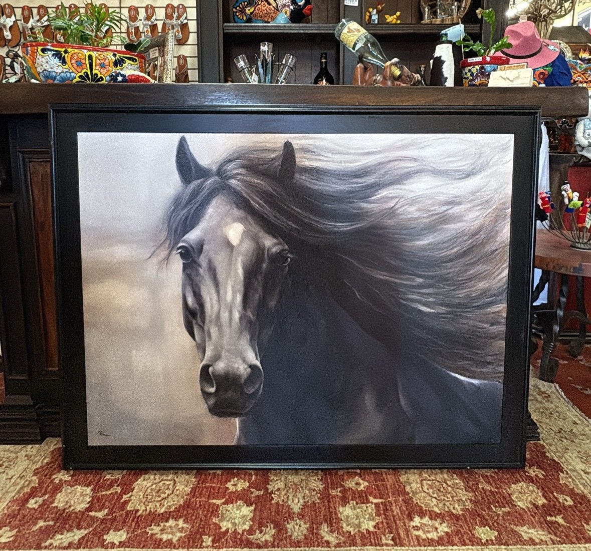 A framed painting of a black horse with a flowing mane, set against a neutral background; the horse is indoors.
