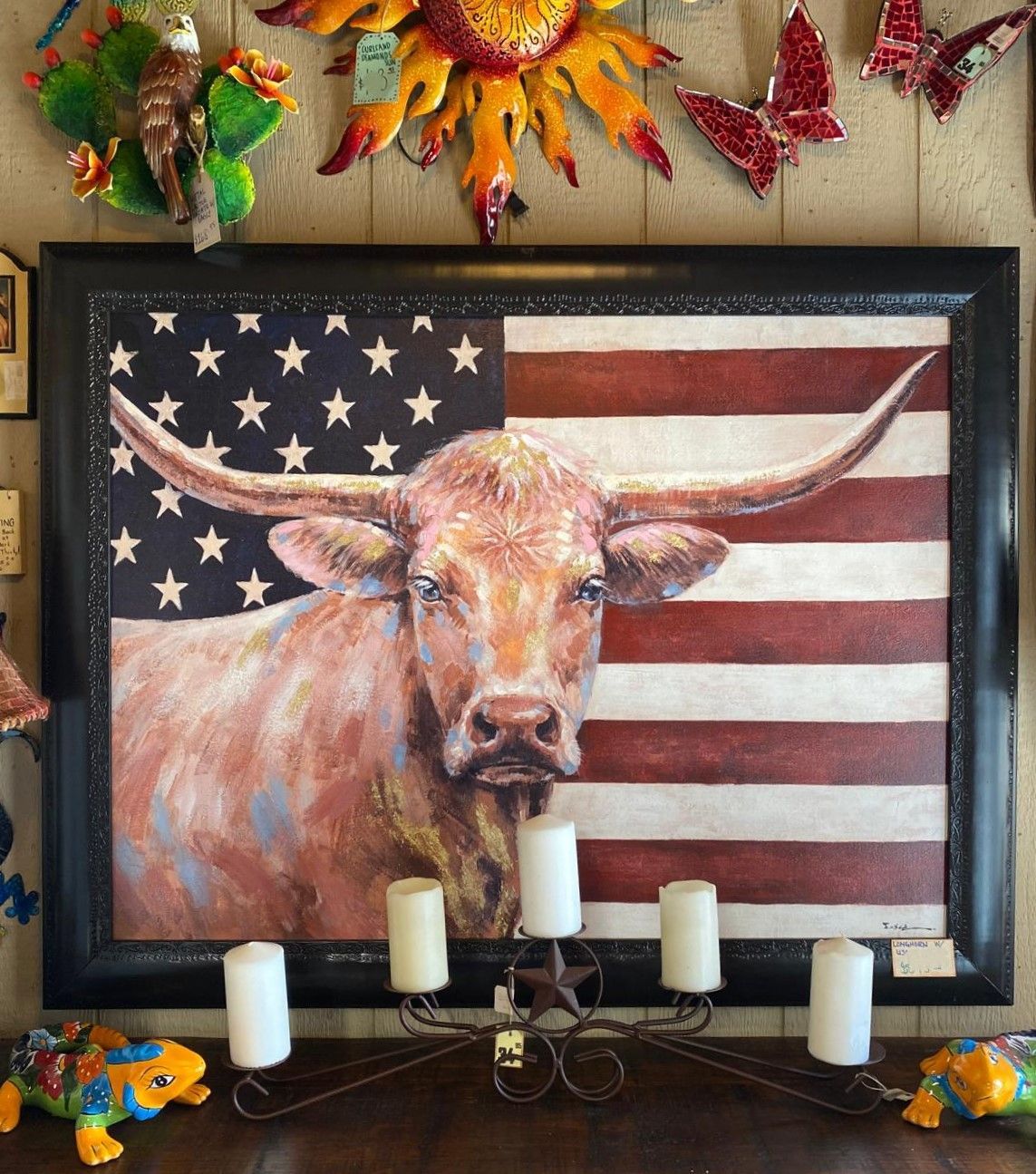 Painting of a longhorn bull with the American flag in the background, framed, with a candelabra below.
