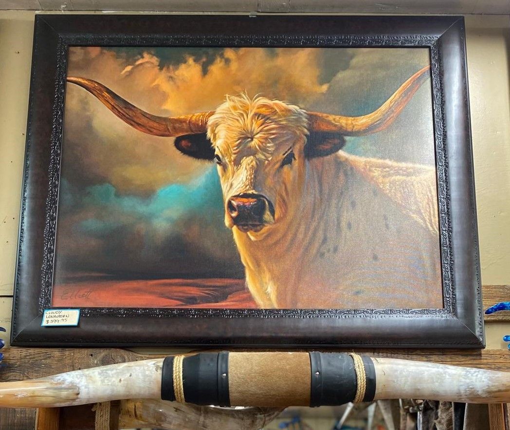 Framed painting of a white longhorn bull with large horns against a colorful sky. A bull horn is visible in the foreground.