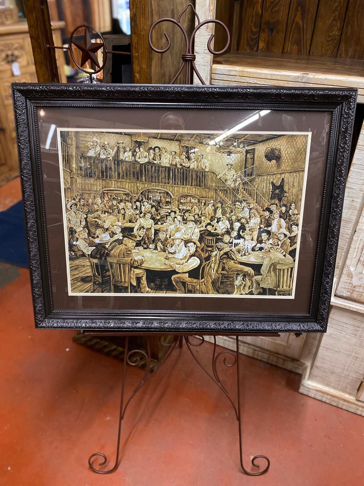 Framed sepia-toned print of a crowded room with a balcony, displayed on a wrought-iron easel.