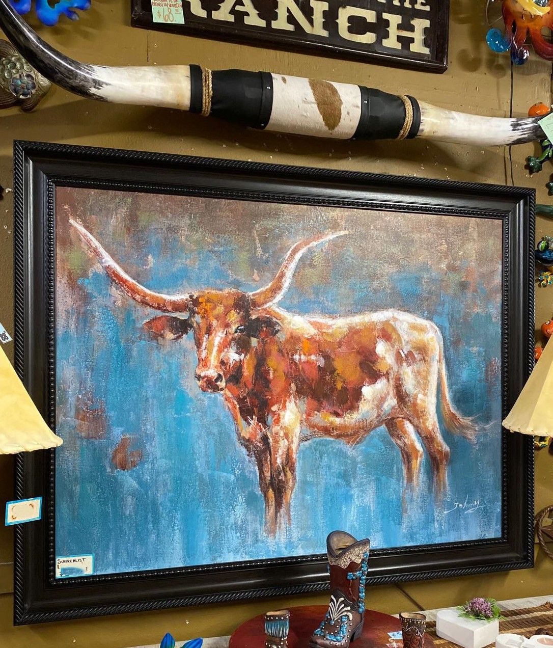 Oil painting of a longhorn steer in front of a blue backdrop, framed in black, with a decorative longhorn horn above it.