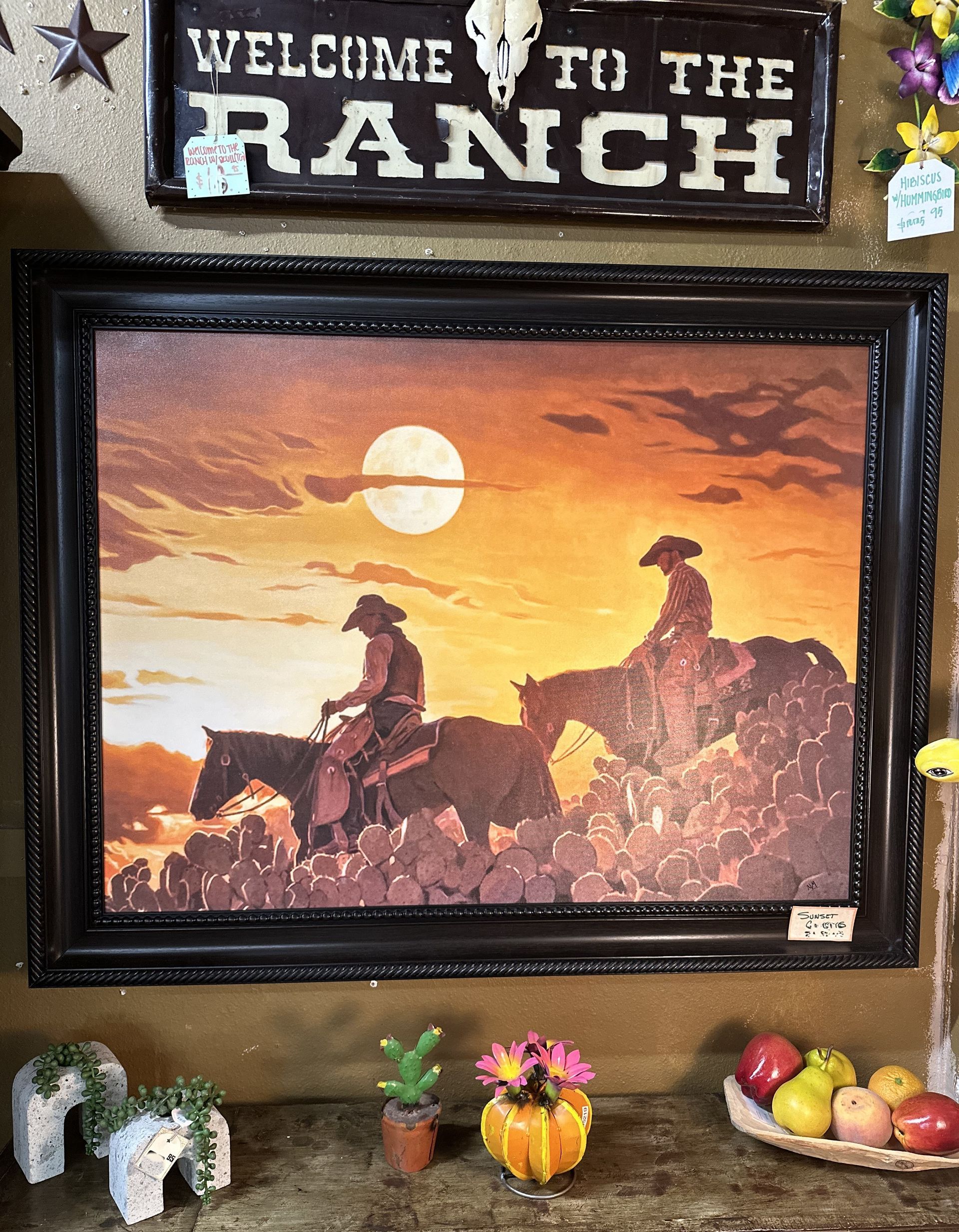 Western-themed art of two cowboys on horseback in sunset, framed and displayed, with Welcome to the Ranch sign above.