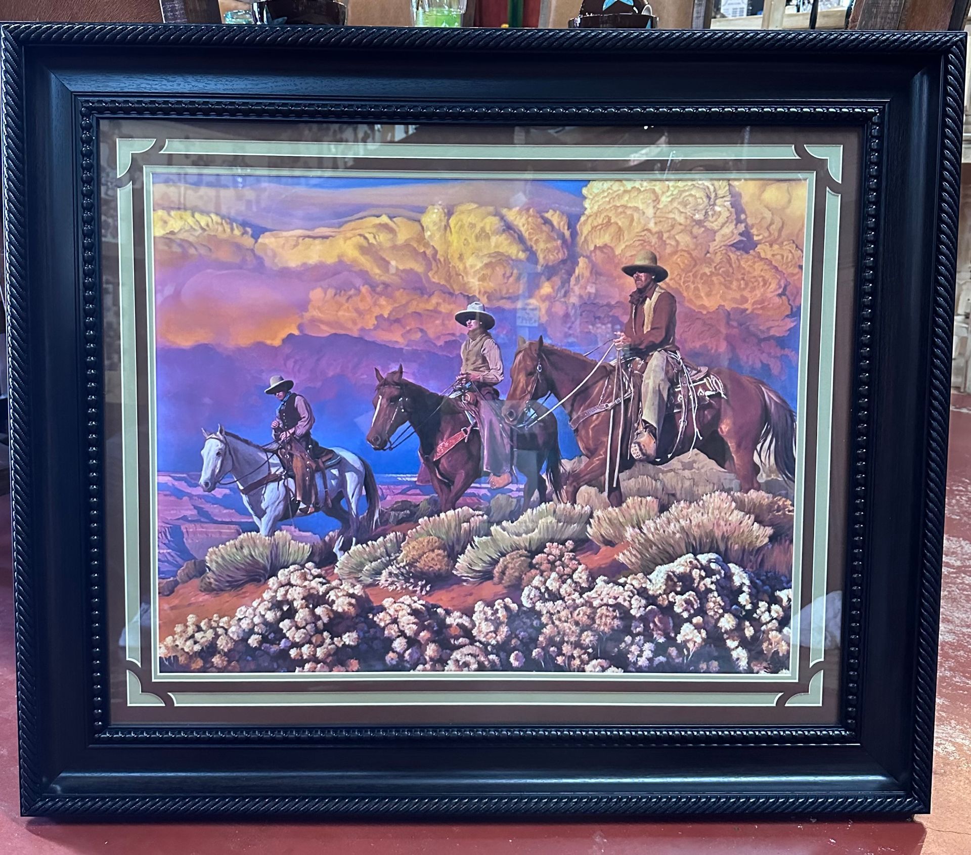 Western art featuring three cowboys on horseback traversing a desert landscape, framed with a dark border.