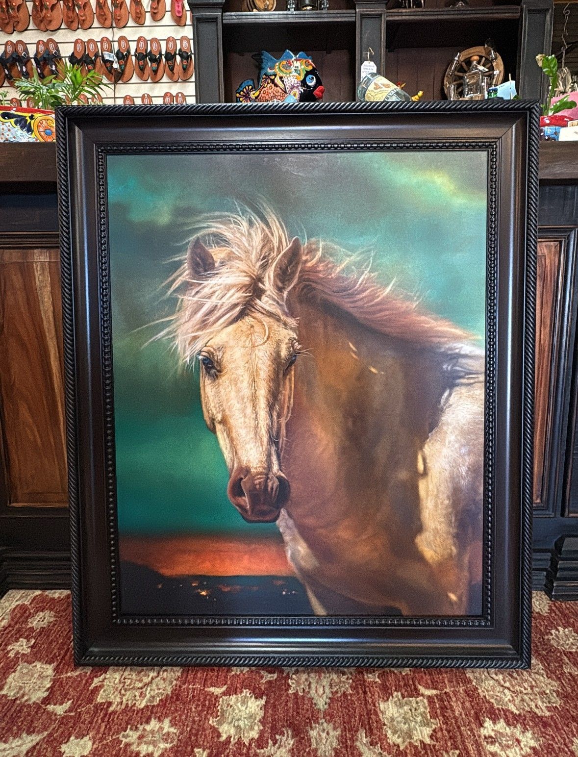 Oil painting of a tan horse with a flowing mane, framed. The horse is against a green and orange backdrop.
