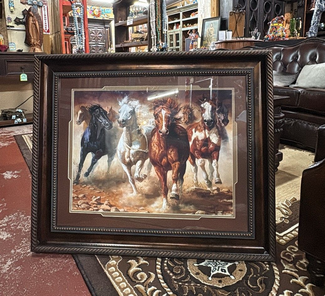 Framed artwork featuring a herd of horses running through a dusty landscape. Browns and whites dominate the color scheme.