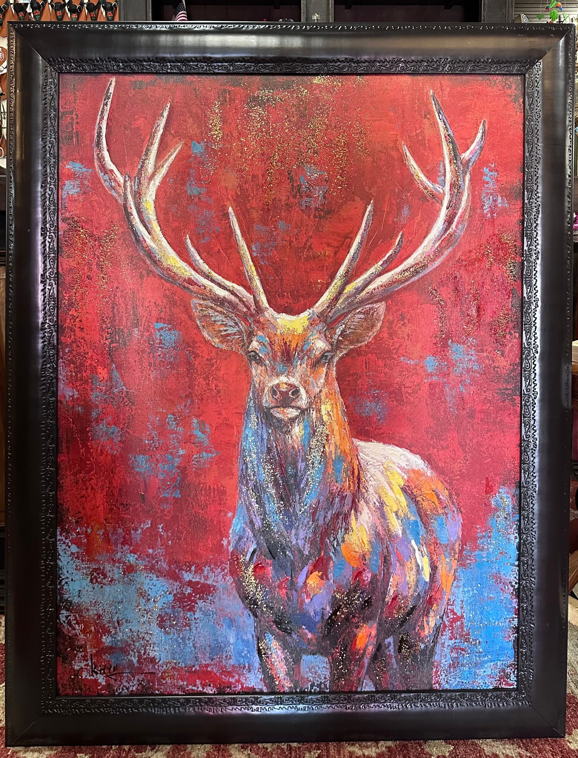 Colorful painting of a deer with large antlers against a red and blue abstract background. Framed artwork.