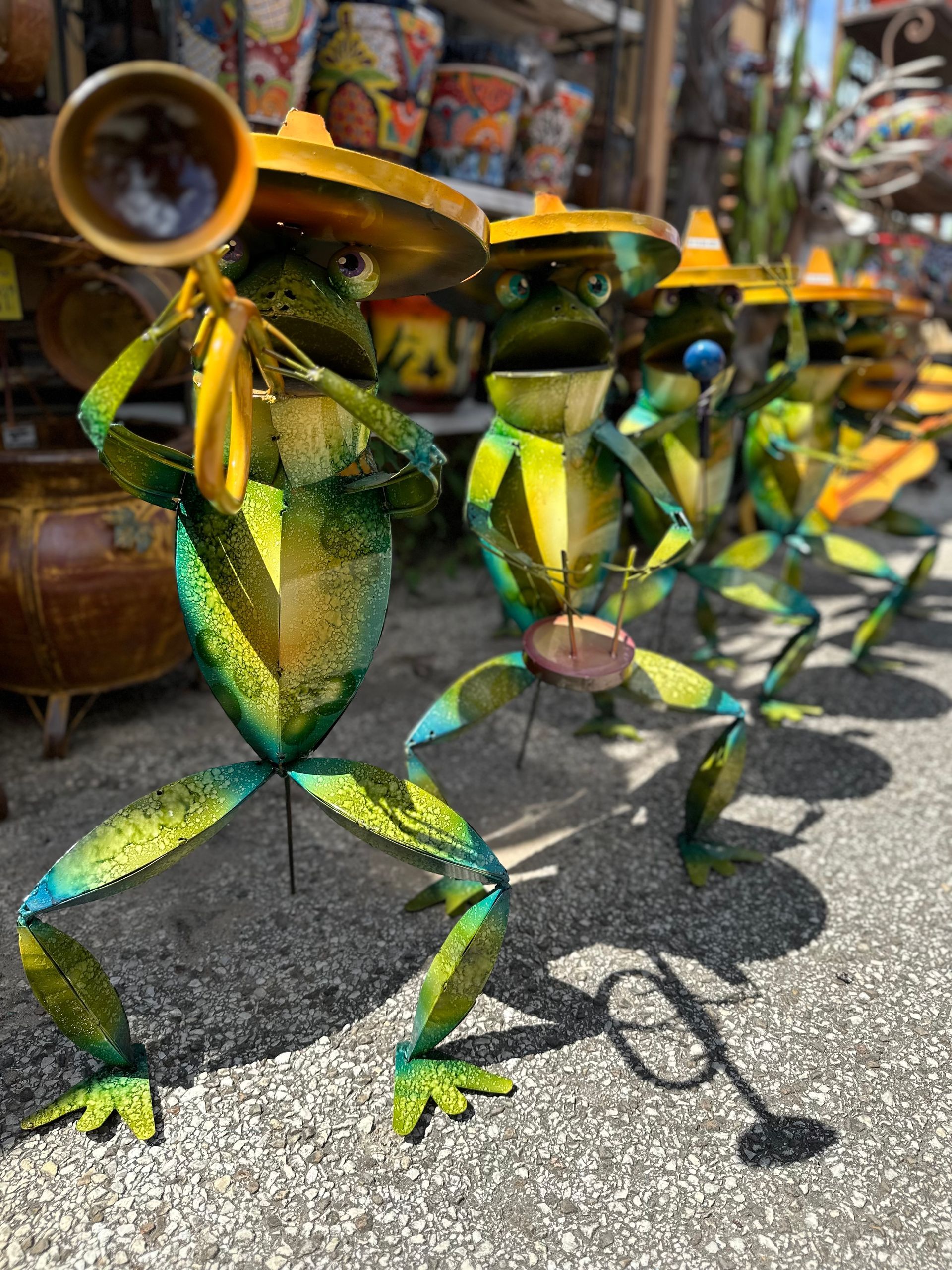 Metal frog band wearing sombreros, playing instruments outdoors, with a blurred background of pottery.