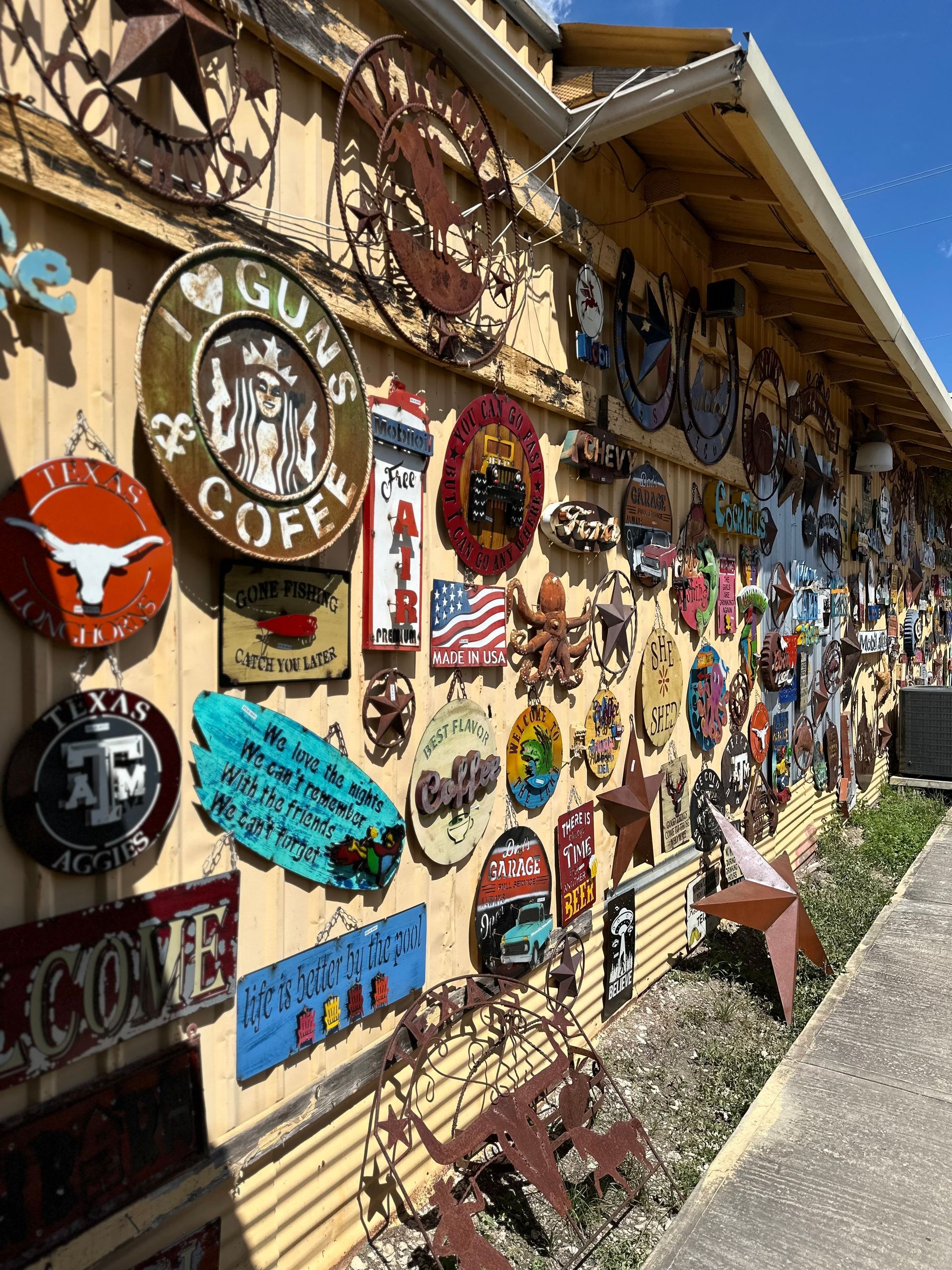 A yellow building exterior covered in various metal signs, with a sidewalk in front.