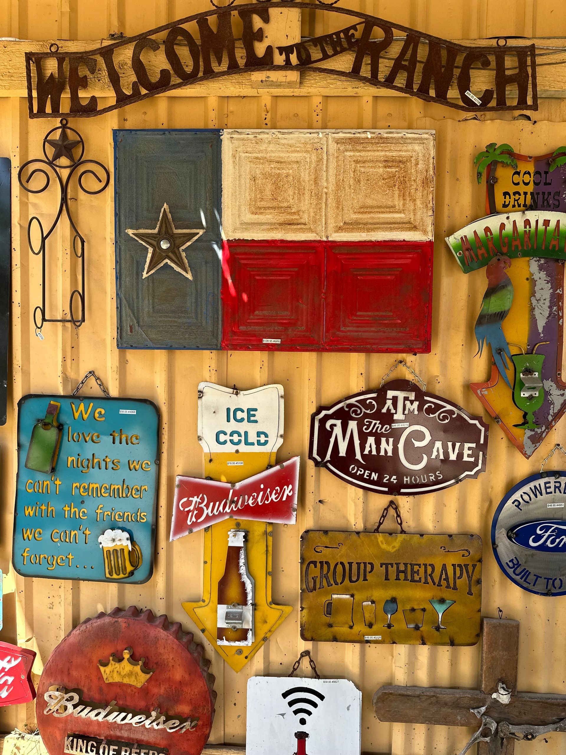Collection of vintage signs including a Texas flag and beer-themed decor, mounted on a yellow wall.