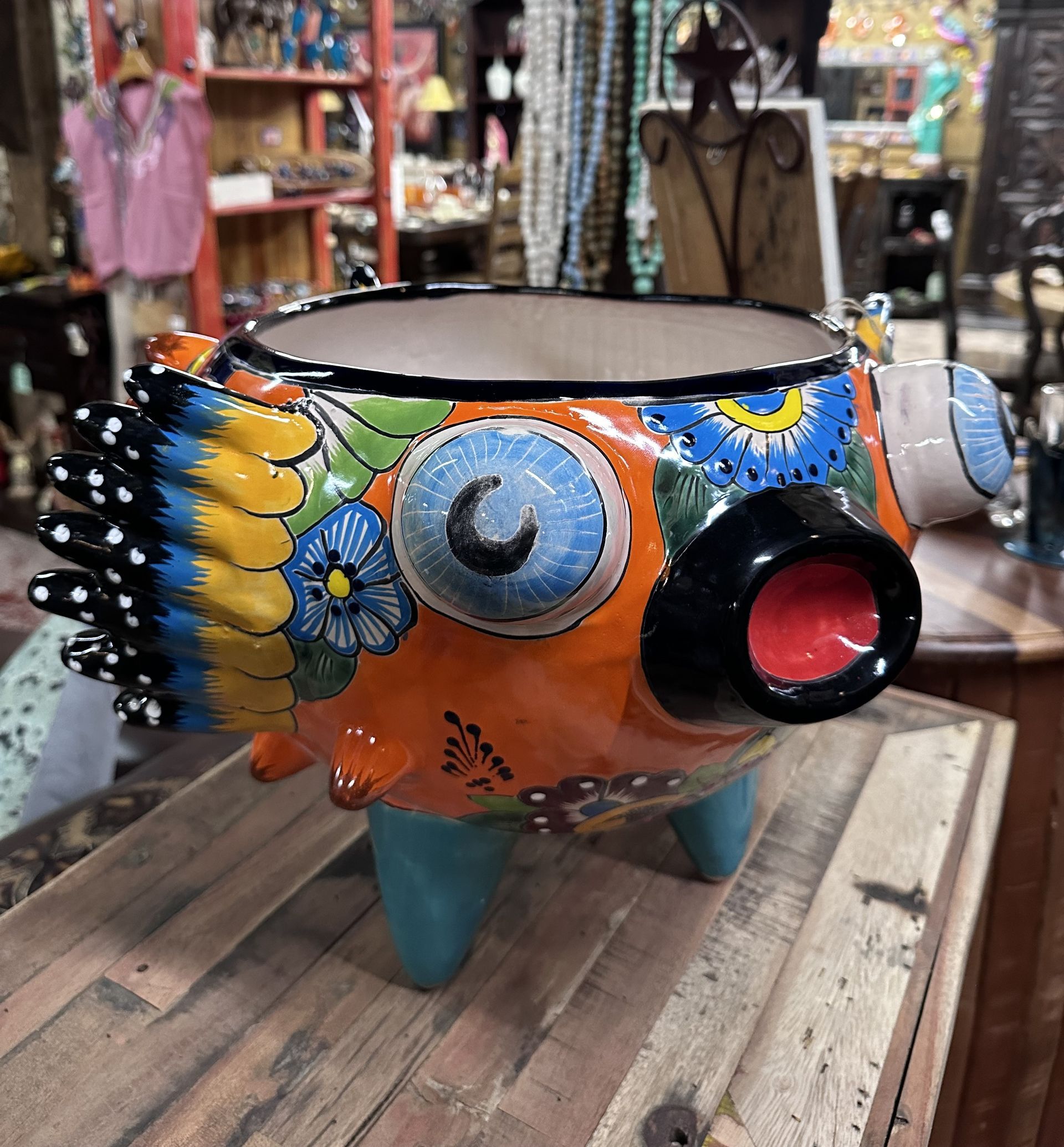 Colorful ceramic planter shaped like a fish, with blue eyes, a black nose, and orange body, sitting on a wooden surface.