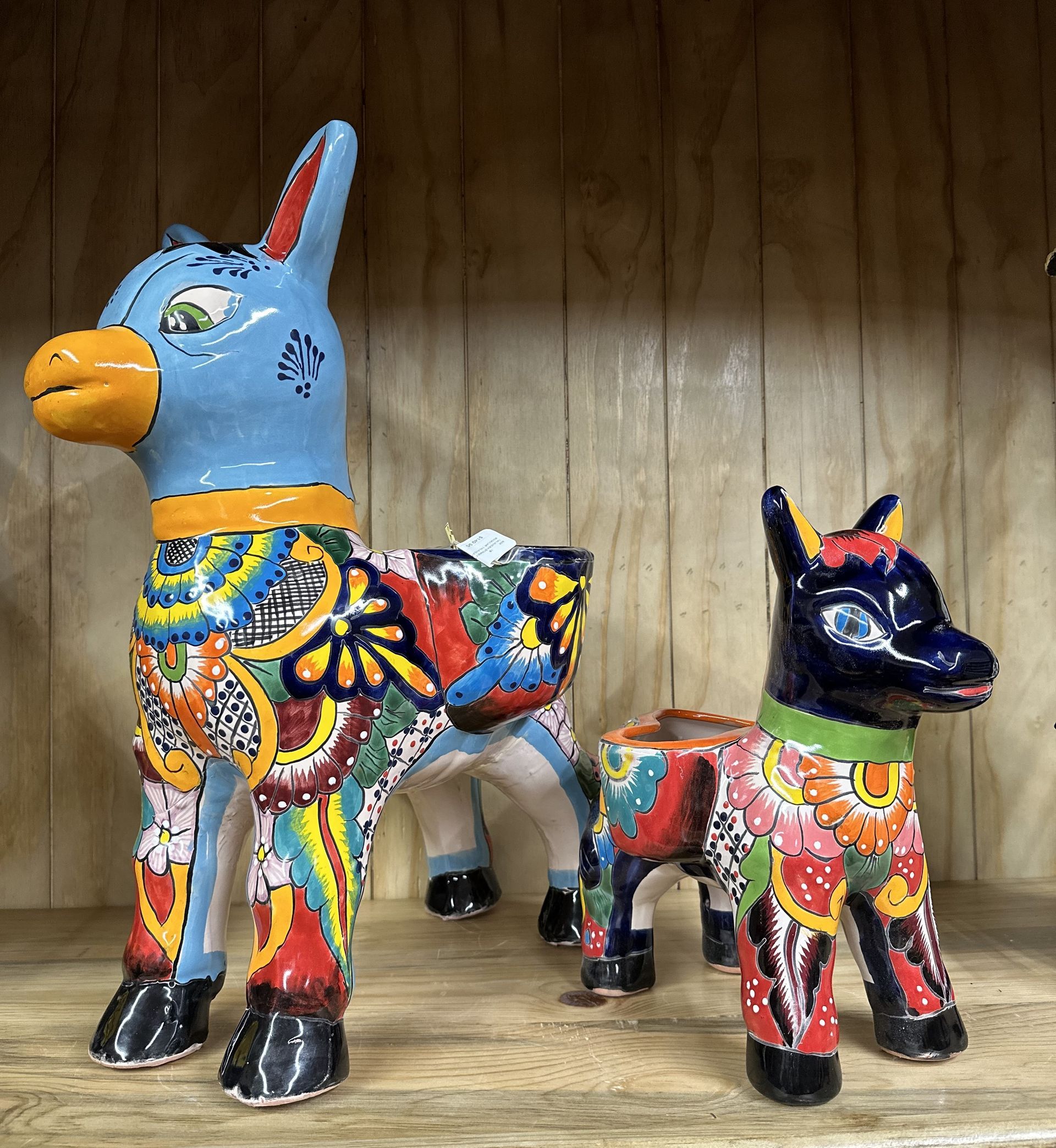 Two colorful, glazed ceramic donkey planters on a wooden shelf, one blue and one dark blue with vibrant floral patterns.