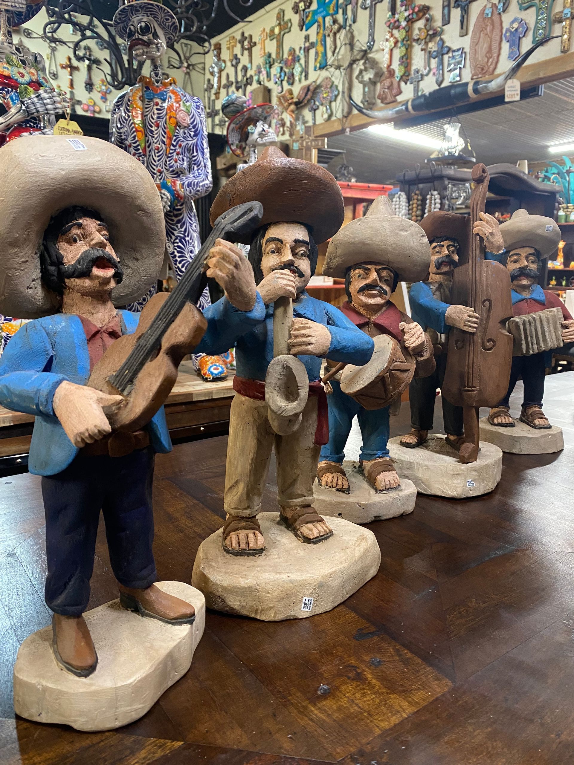 Mariachi band figurines in a shop, wearing sombreros and playing instruments. Each has a mustache and is standing on a stone base.