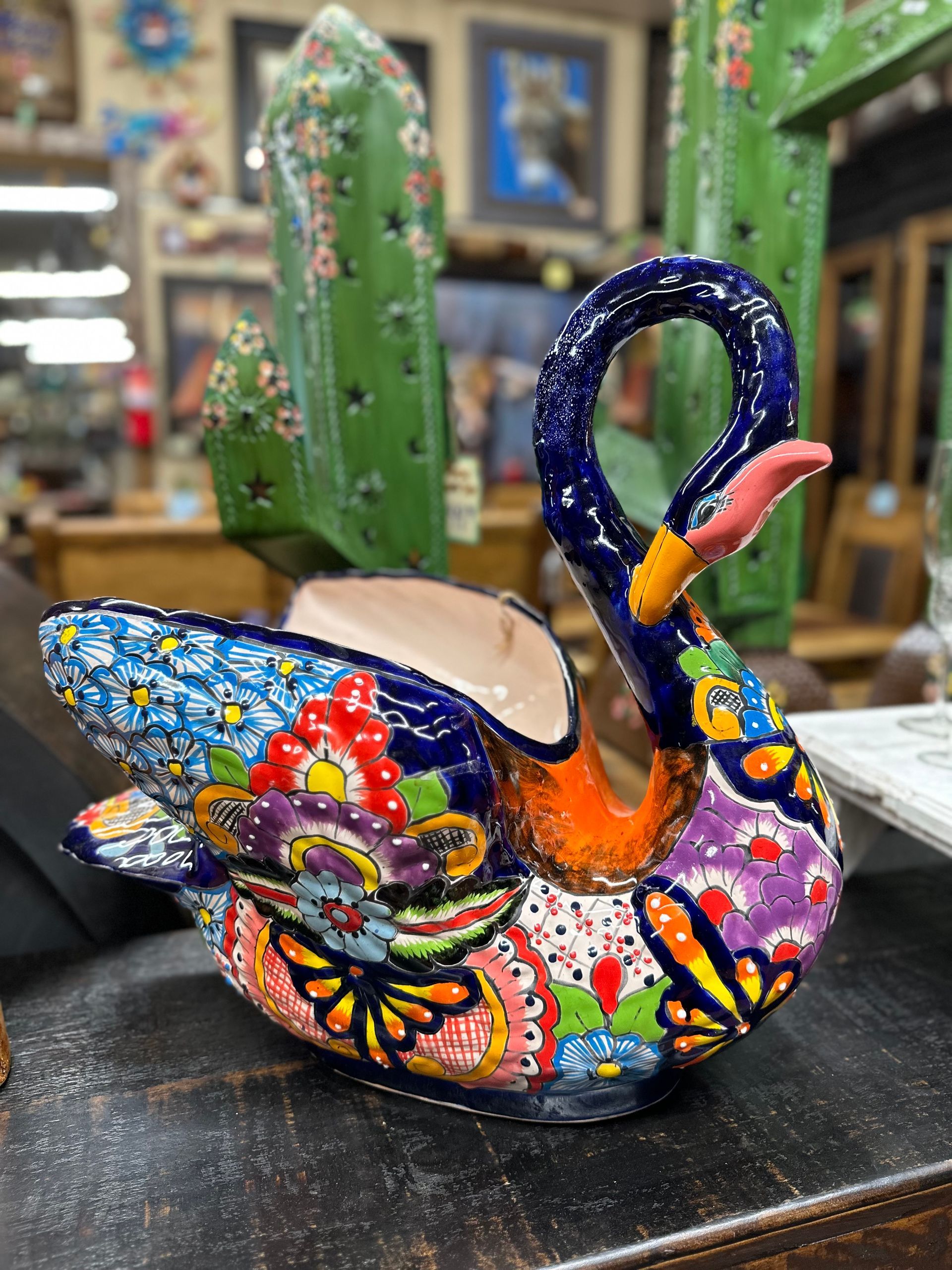 A colorful, ceramic swan planter with an open back, decorated in blues, oranges, and reds, set against a blurry antique store background.