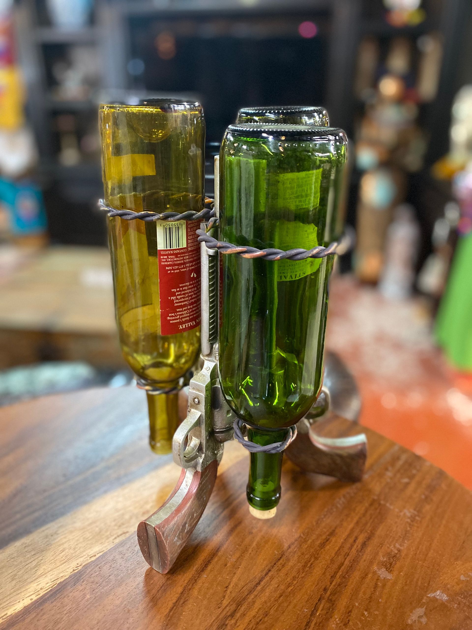 A wine bottle holder in the shape of a gun with three wine bottles. The bottles are green and the holder is metallic.