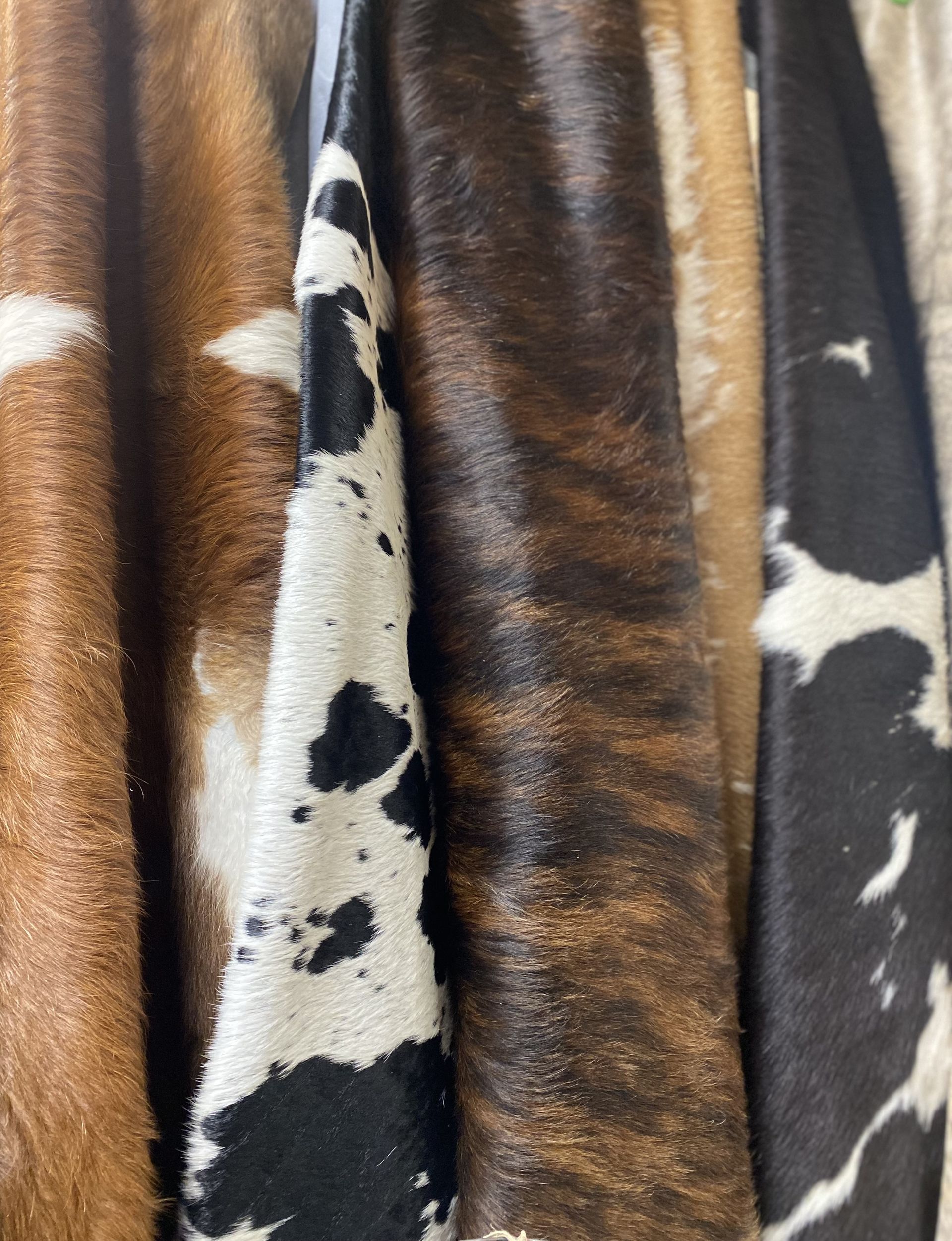 Close-up of several cowhide pieces with distinct patterns: brown and white, black and white, and brown brindle.
