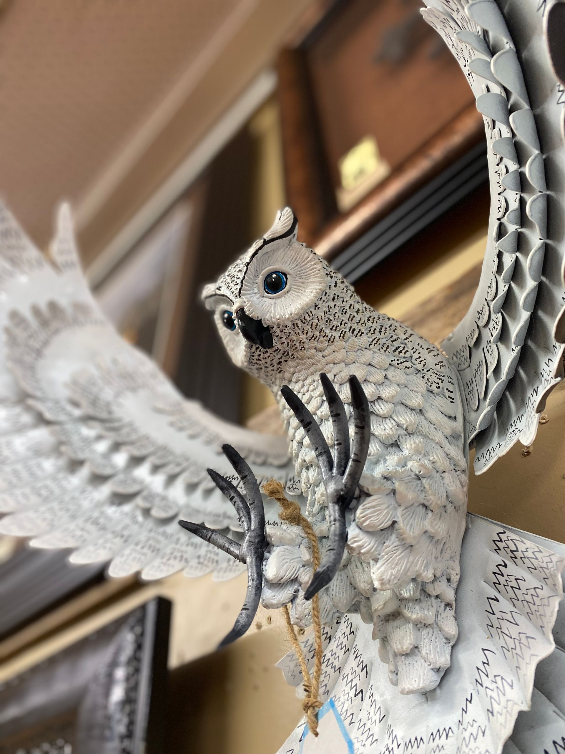 White owl sculpture with outstretched wings, perched on a branch. The owl has black and white markings with a focused gaze.