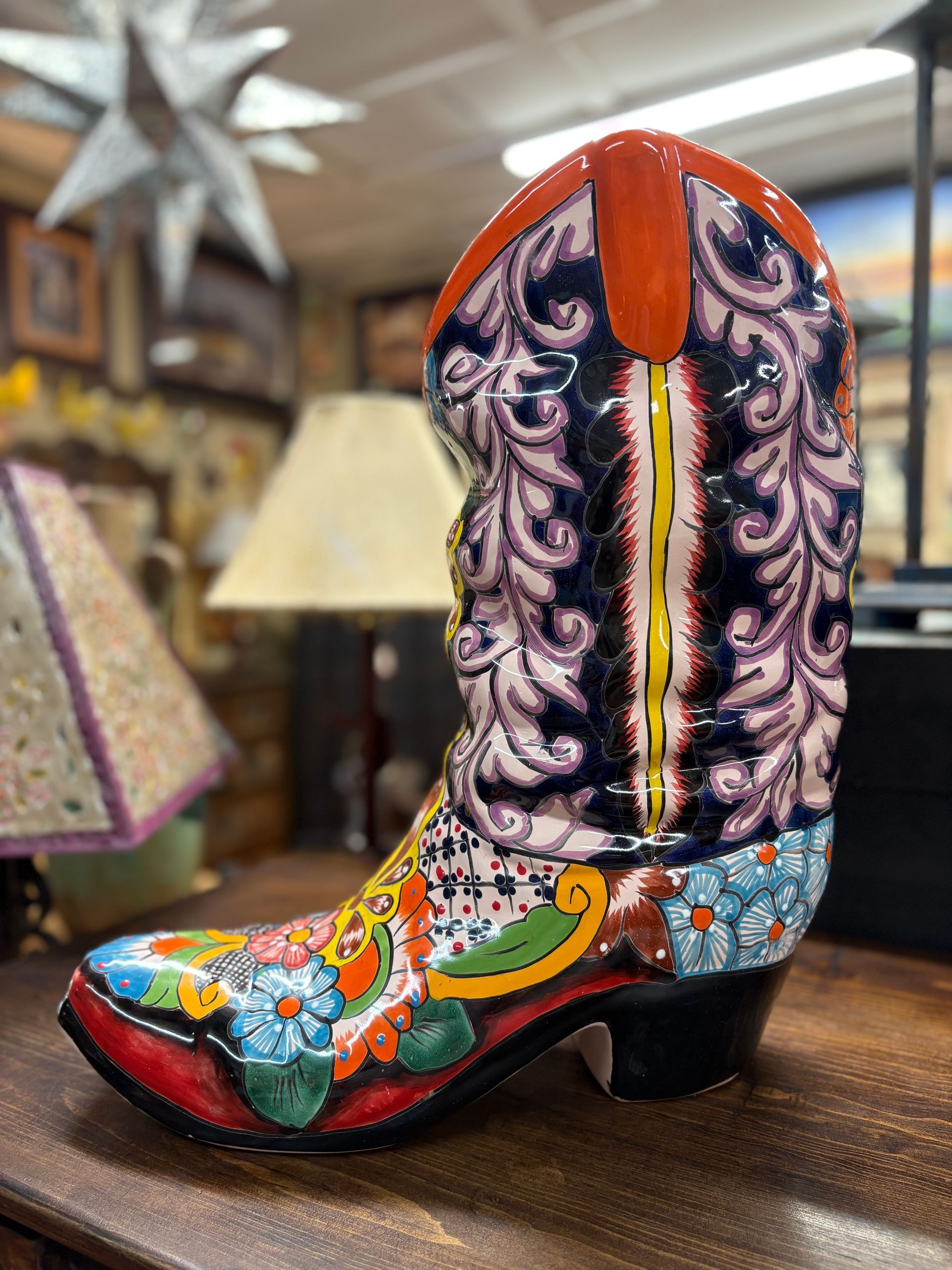 Colorful, ceramic cowboy boot with floral and swirling patterns, set on a wooden surface in a shop.