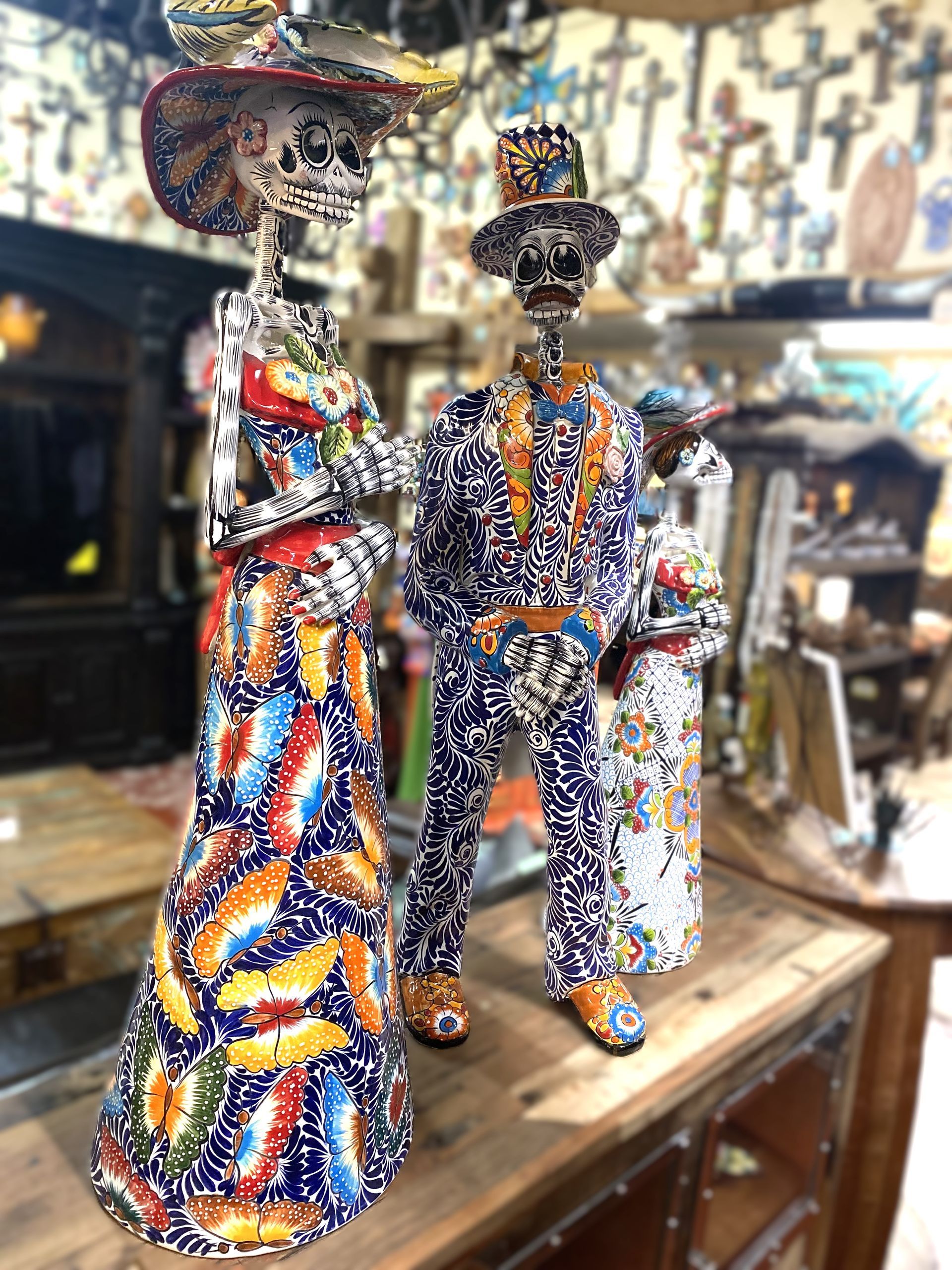Colorful skeleton figures in a shop setting. The figures are dressed in patterned clothes and hats, likely for Day of the Dead.
