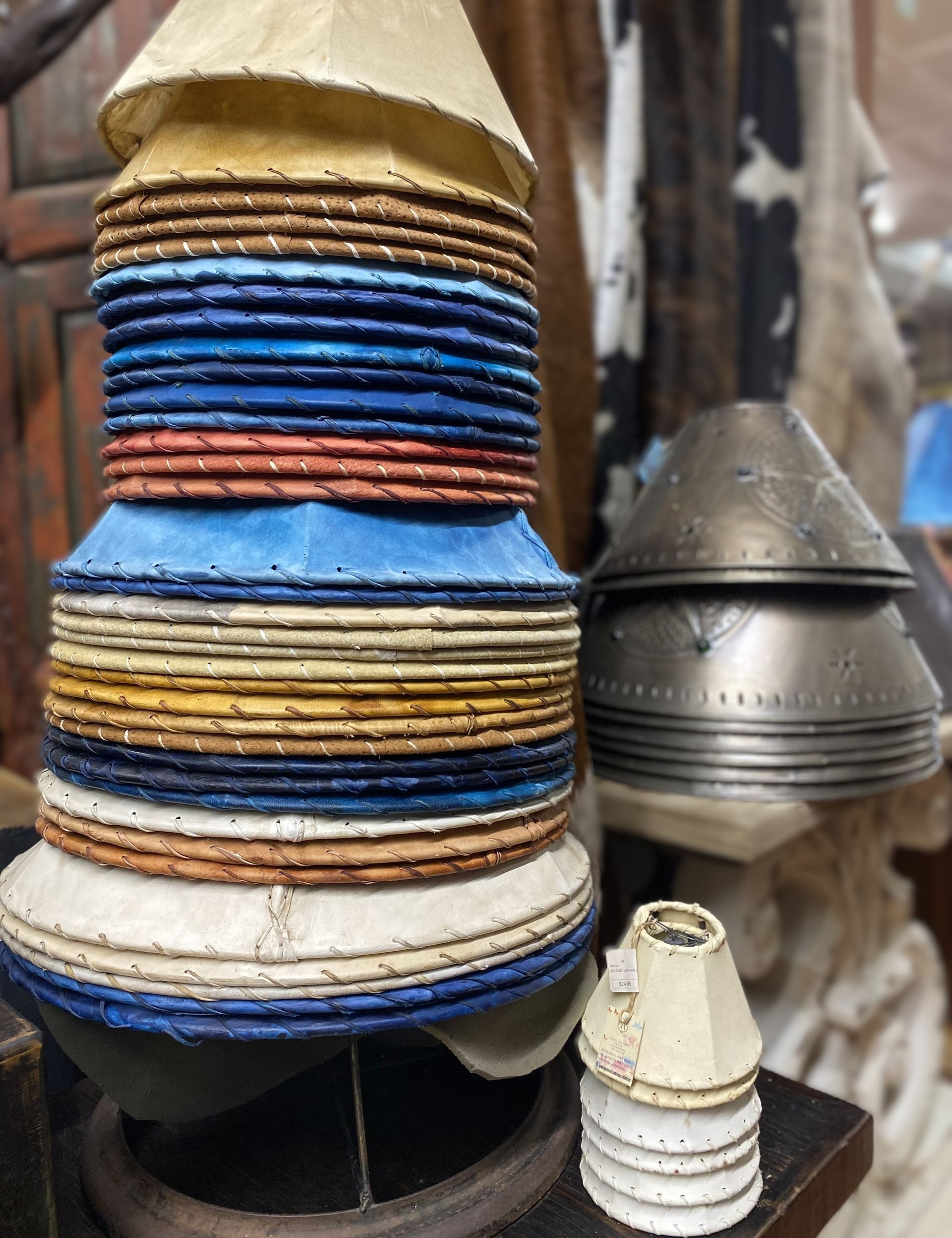 Stacks of colorful, inverted paper lampshades and a metal lampshade.  Setting appears to be a workshop or antique store.