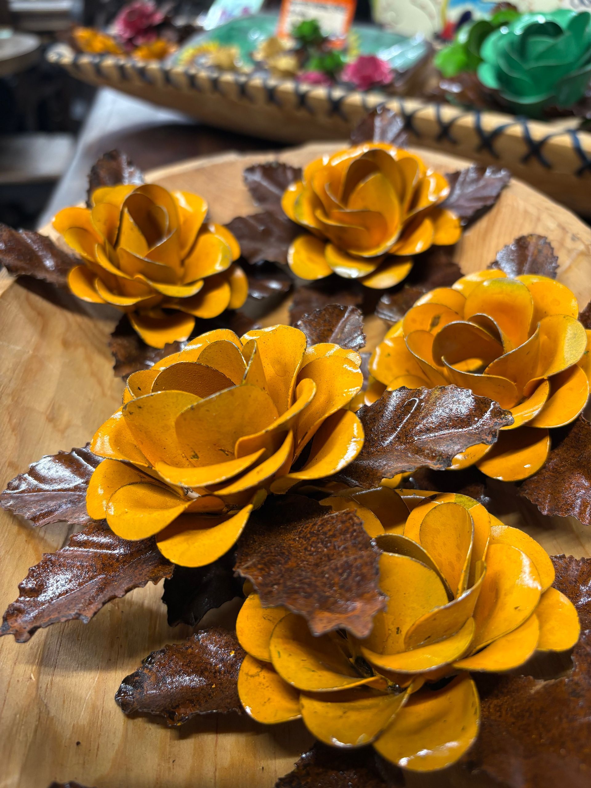 Close-up of five handmade yellow metal roses with brown leaves, arranged on a wooden surface.