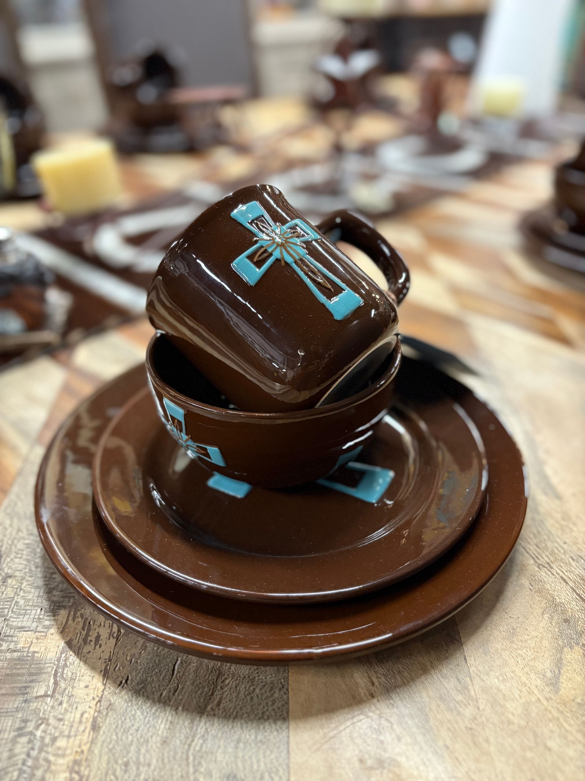 Brown ceramic dinnerware set with turquoise cross design; includes plates, bowl, and a mug.