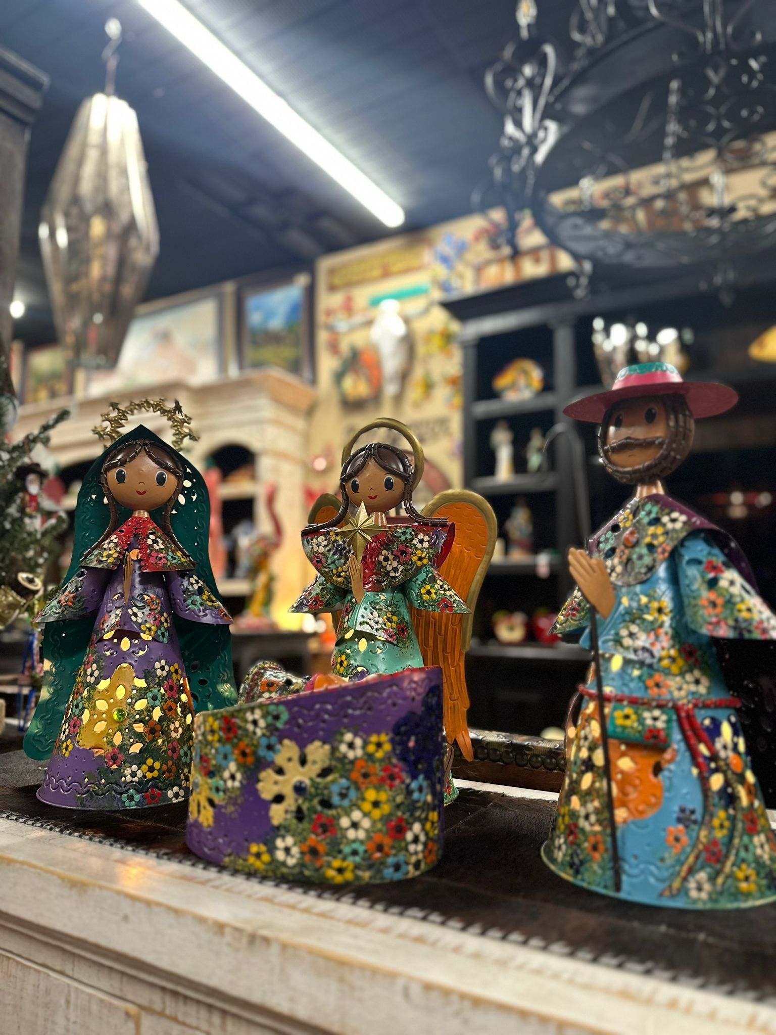 Three brightly painted folk art figures: Mary, an angel, and a man, decorated with floral patterns, on a shelf.