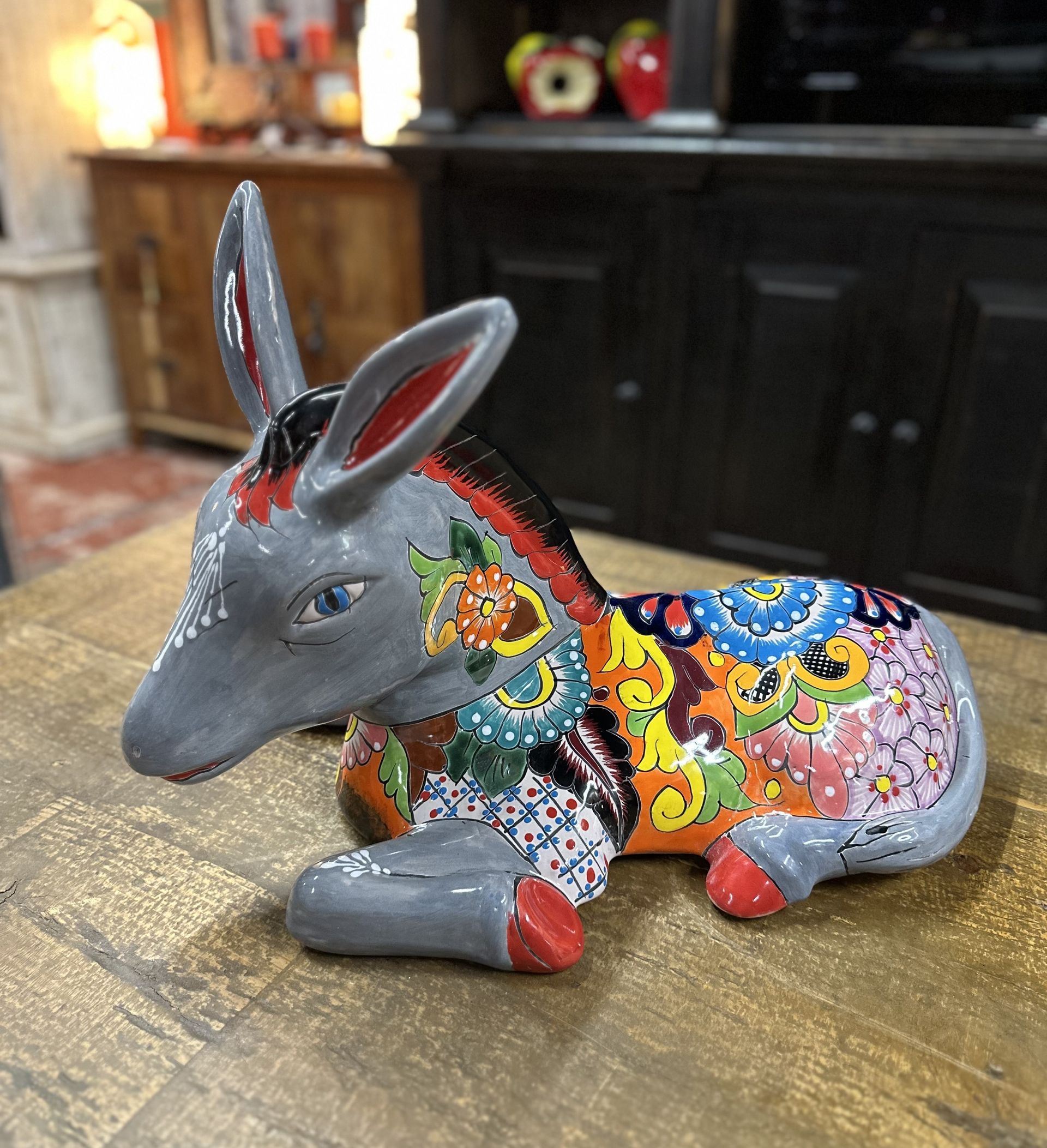 Gray ceramic donkey figurine with colorful mosaic-like patterns on its back, resting on a wooden table.