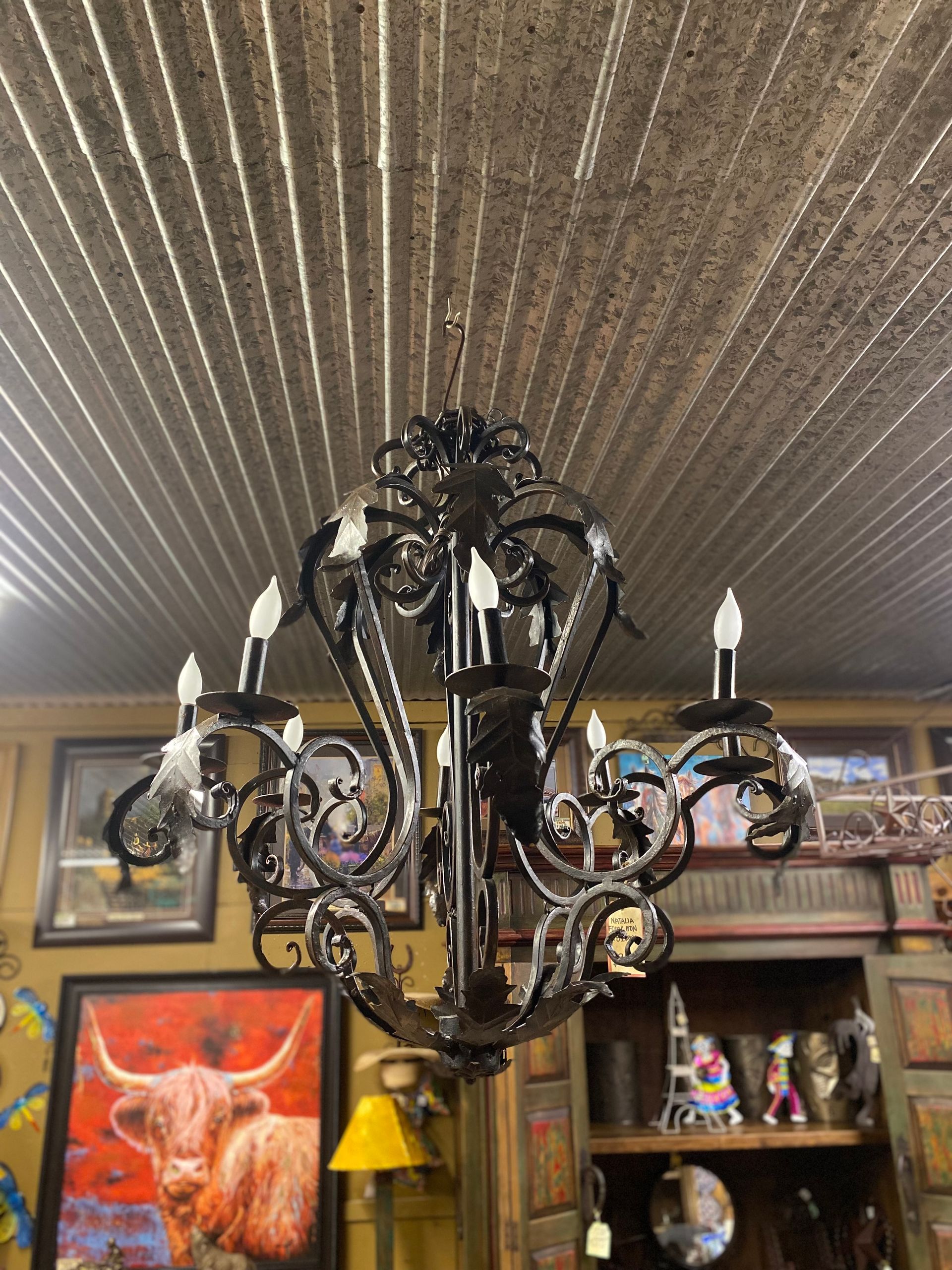 Black wrought iron chandelier hanging from a corrugated metal ceiling, displaying six candelabra bulbs.
