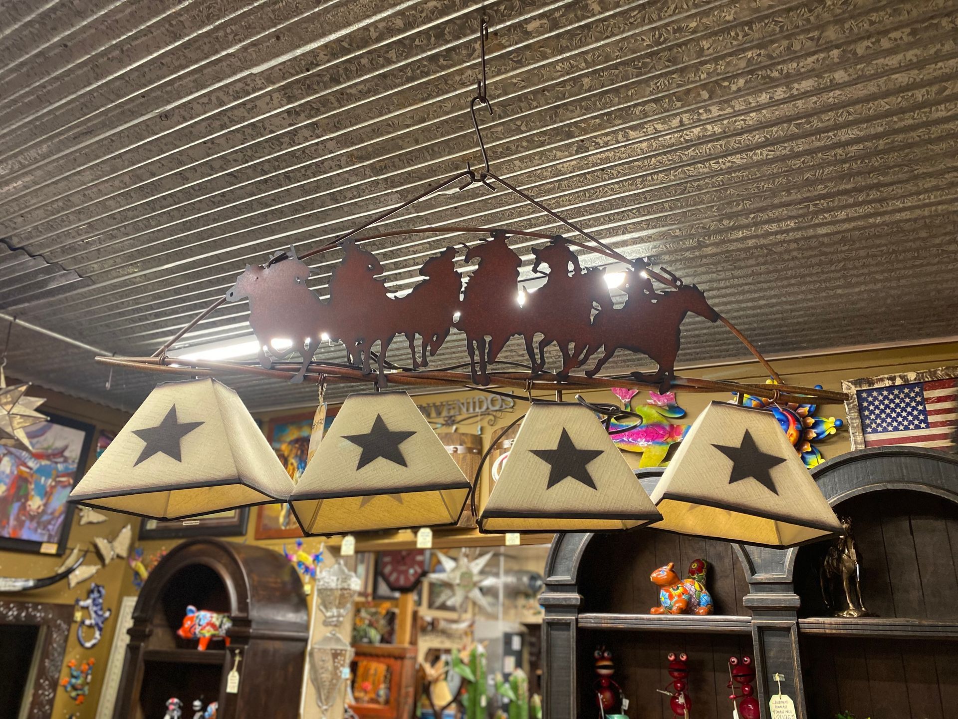 A rustic chandelier with cowboy silhouettes and star-shaped lampshades hangs in a shop filled with decor.