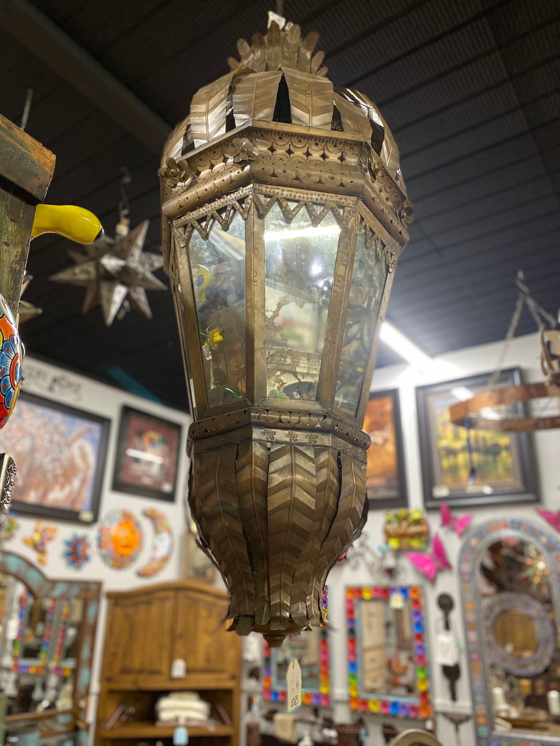Antique brass lantern with glass panels, hanging in a shop filled with various decorative items.