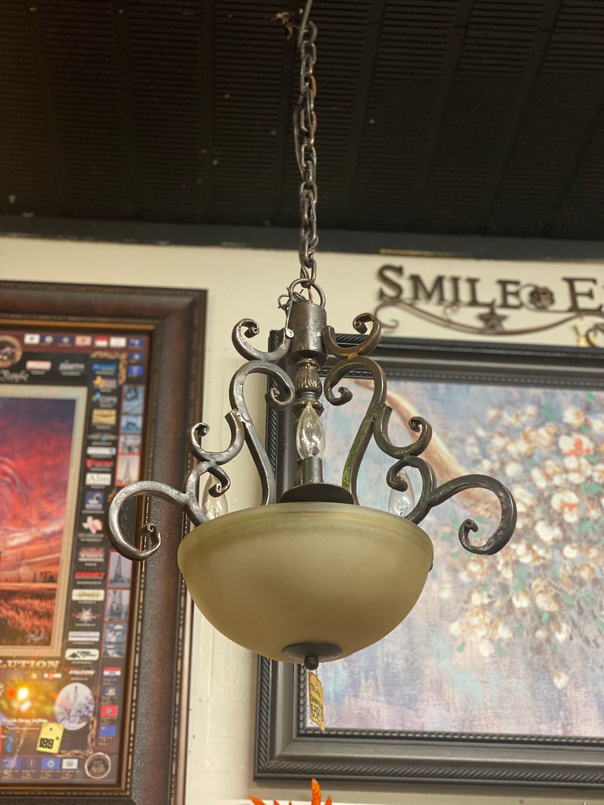 Bronze chandelier with frosted glass shade hanging from a chain, surrounded by decorative ironwork.