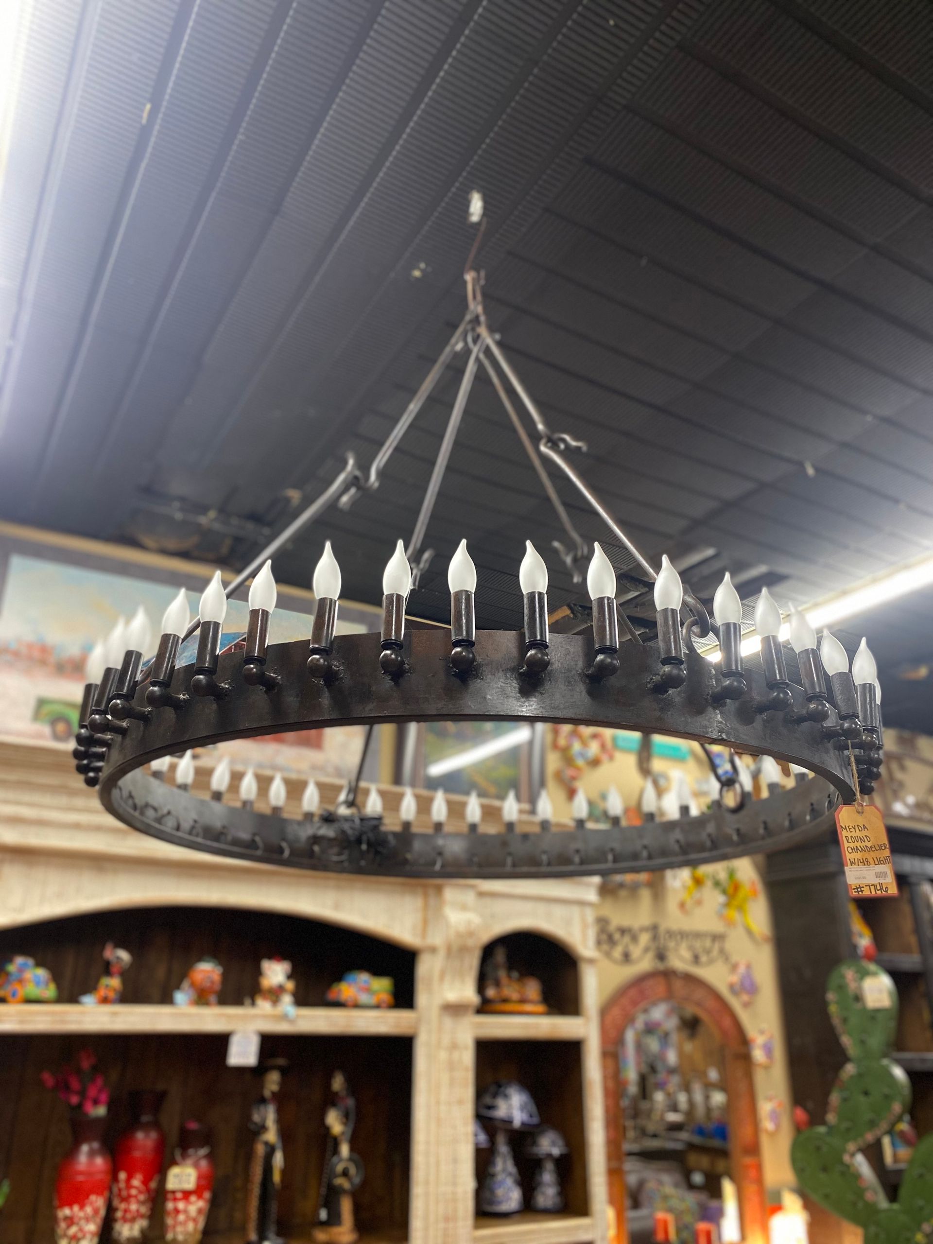 A large, circular black chandelier with many candle-shaped lights hangs in a shop filled with Mexican decor.