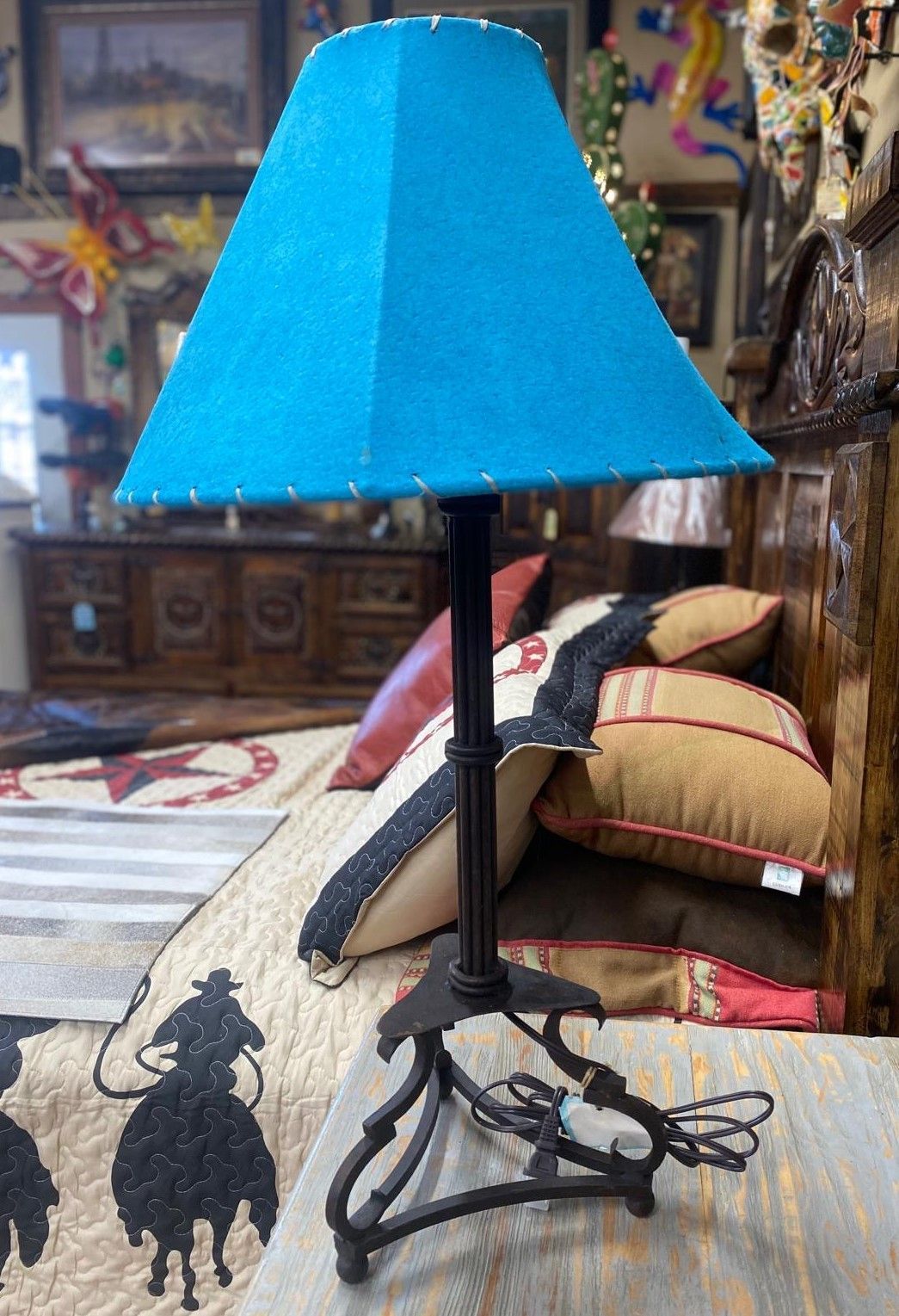 A turquoise lampshade atop a black metal lamp on a bed, with pillows and a quilt visible.
