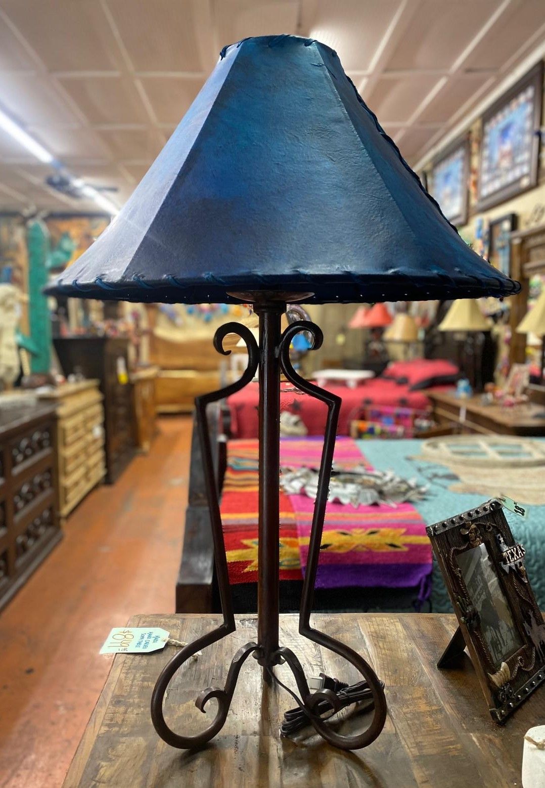 A rustic table lamp with a dark blue lampshade and wrought iron base sits on a wooden table.