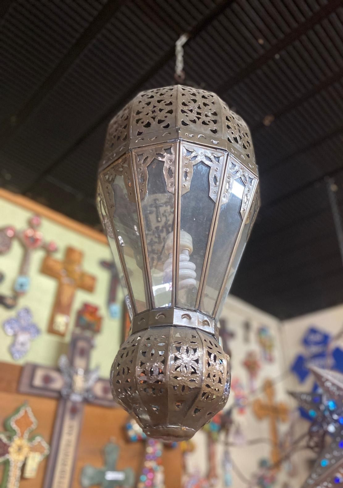Ornate metal lantern hanging indoors with a bulb inside, displaying decorative cut-out patterns.