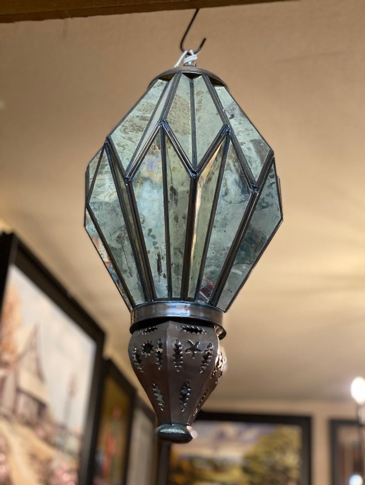 Ornate, geometric glass lantern hanging from a hook; antique silver and copper color.