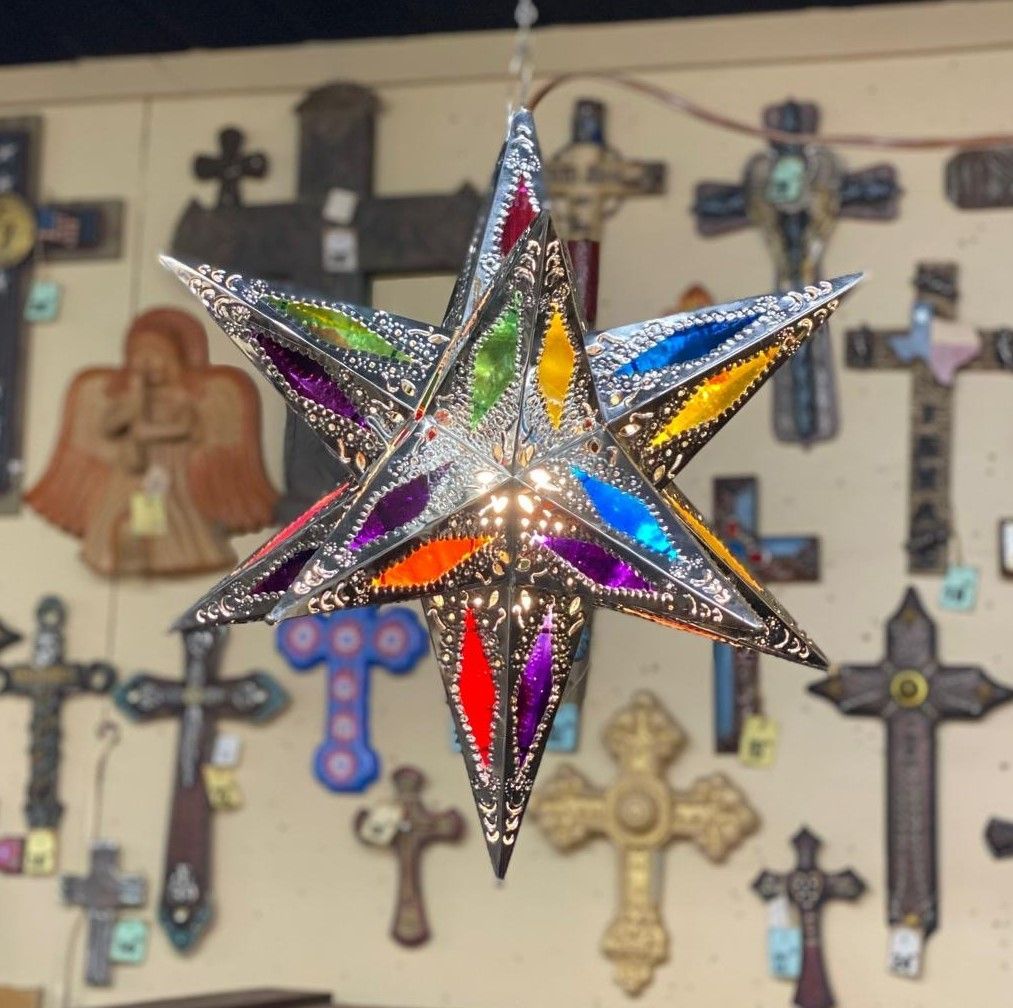 Silver star-shaped lantern with colorful stained glass panels, hanging in front of a wall of crosses.