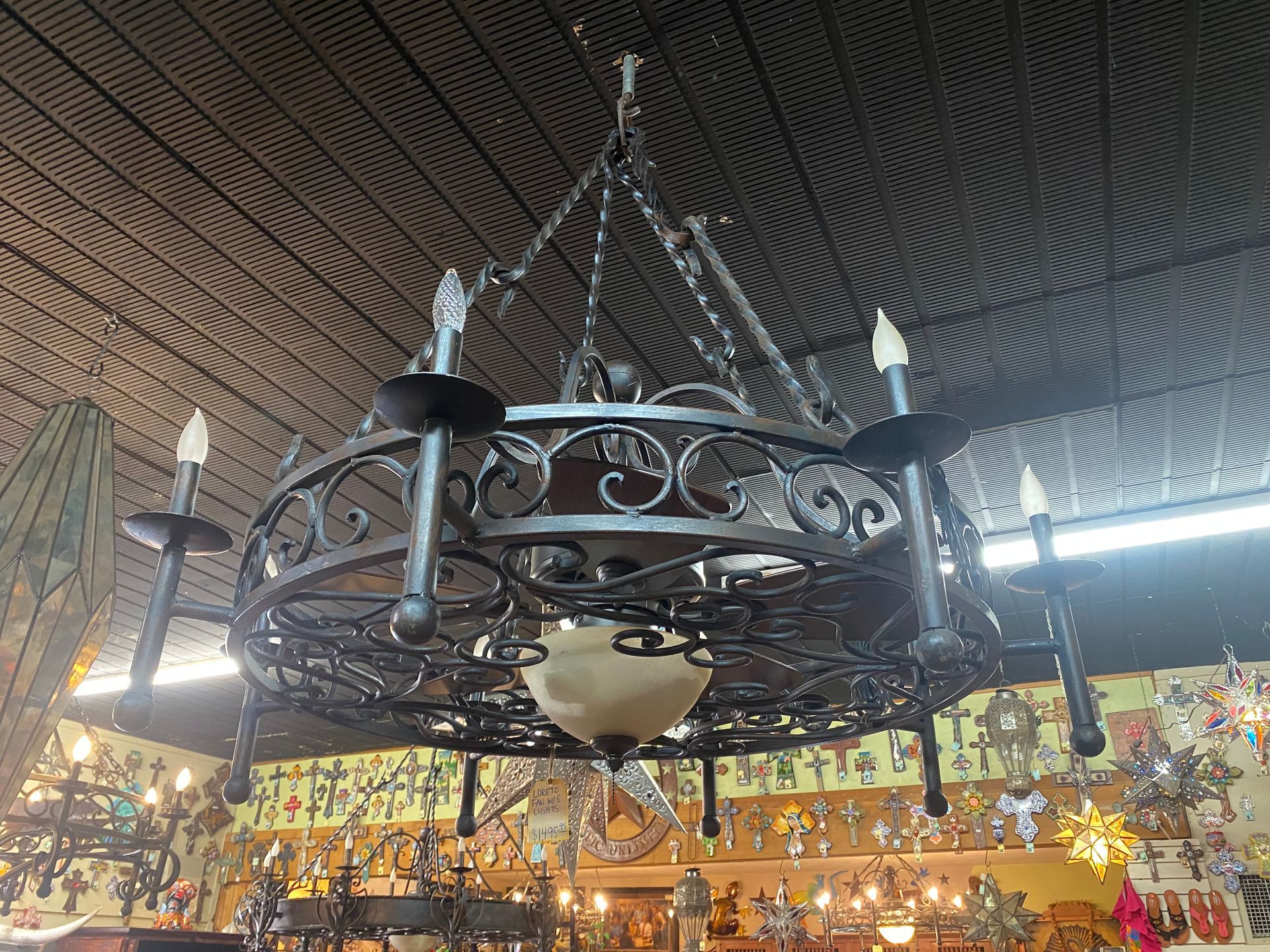 Ornate wrought-iron chandelier with faux candle lights hanging in a shop. Ceiling has a textured pattern.