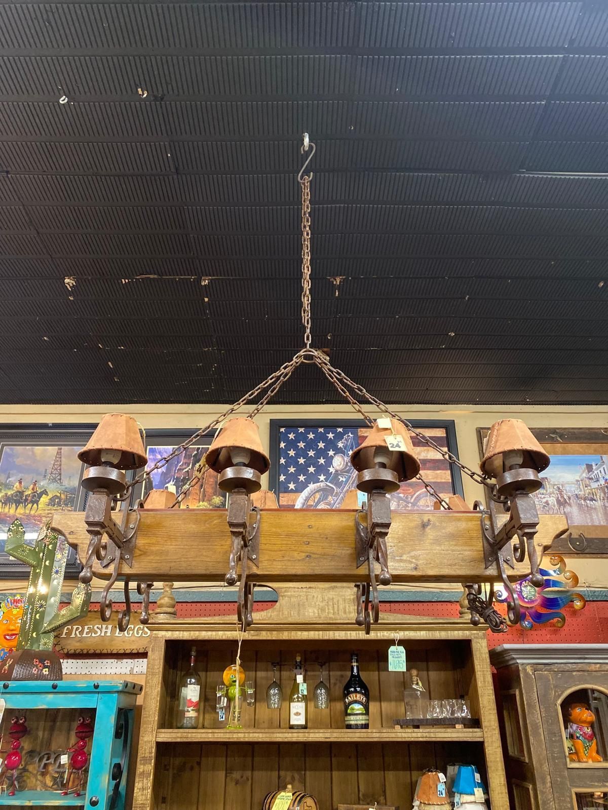 A rustic, western-style chandelier with four terracotta-shaded lights hangs above a wooden shelf with display items.