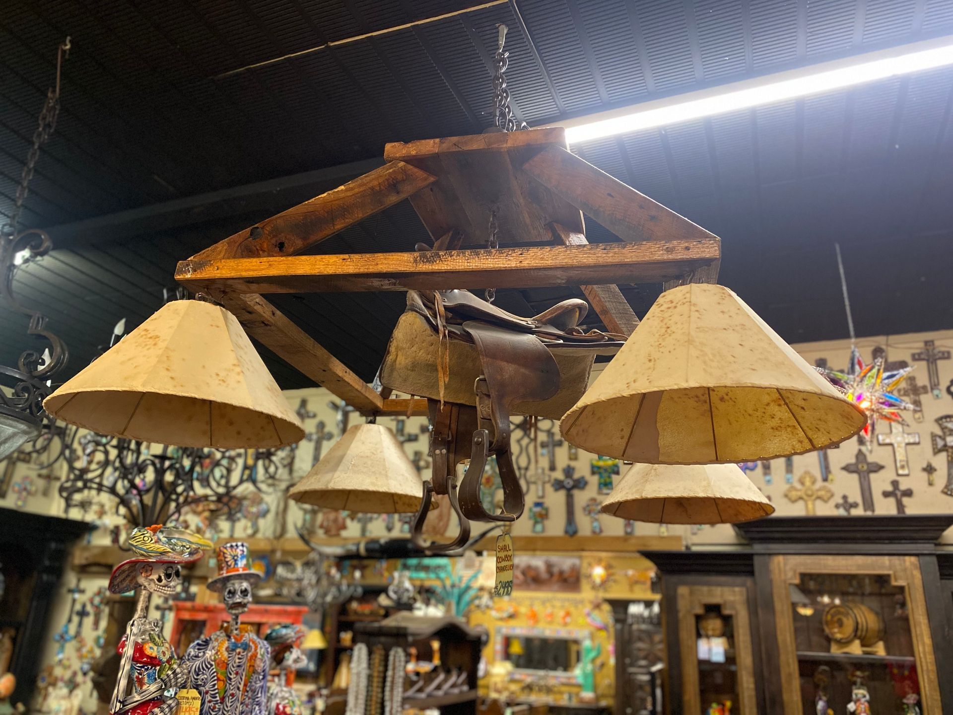 Rustic chandelier featuring a saddle and four lampshades. It's made from wood, with a dark interior background filled with decor.