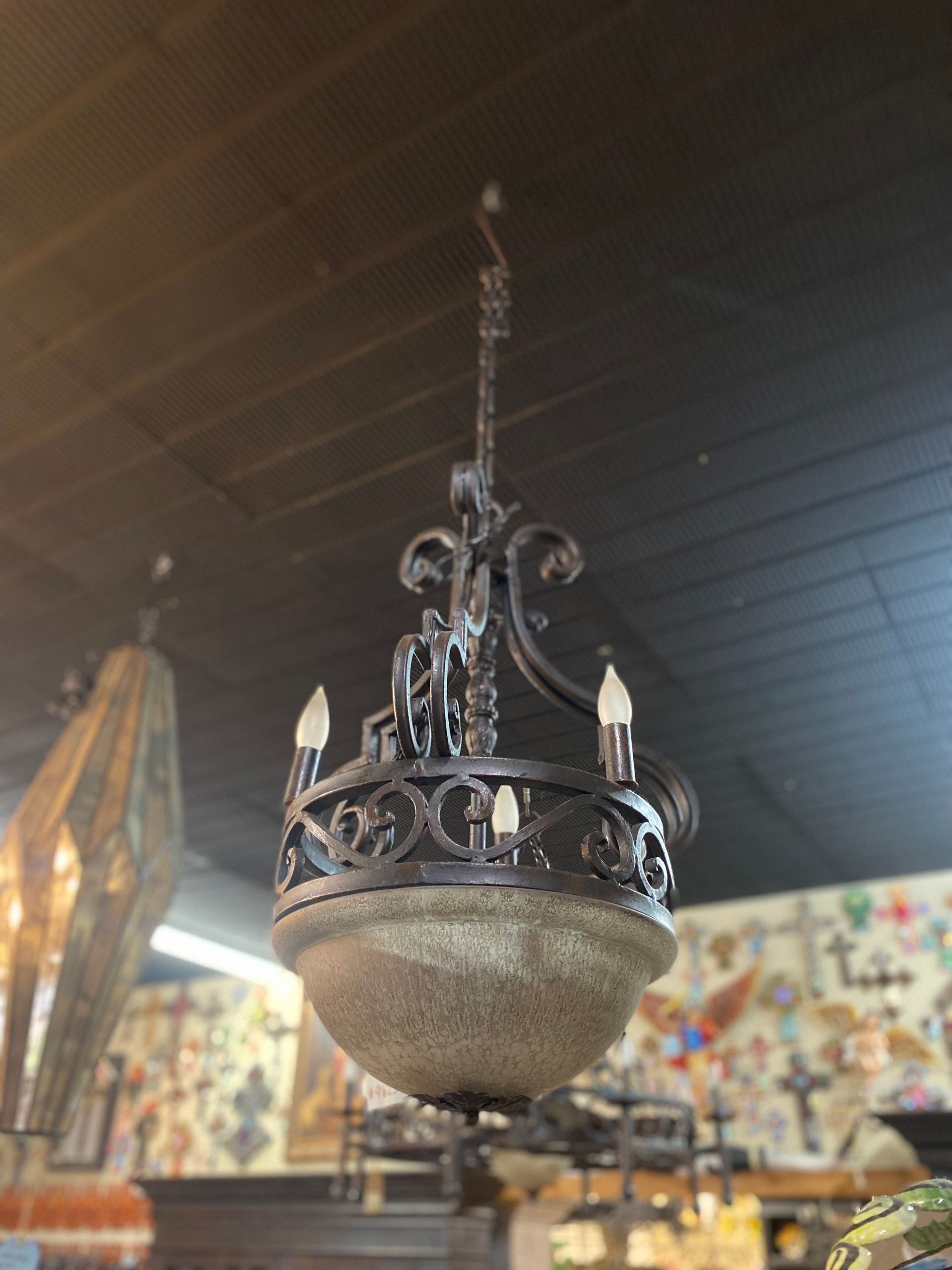 Ornate wrought-iron chandelier with a speckled, globe-shaped glass shade hanging from a dark ceiling.