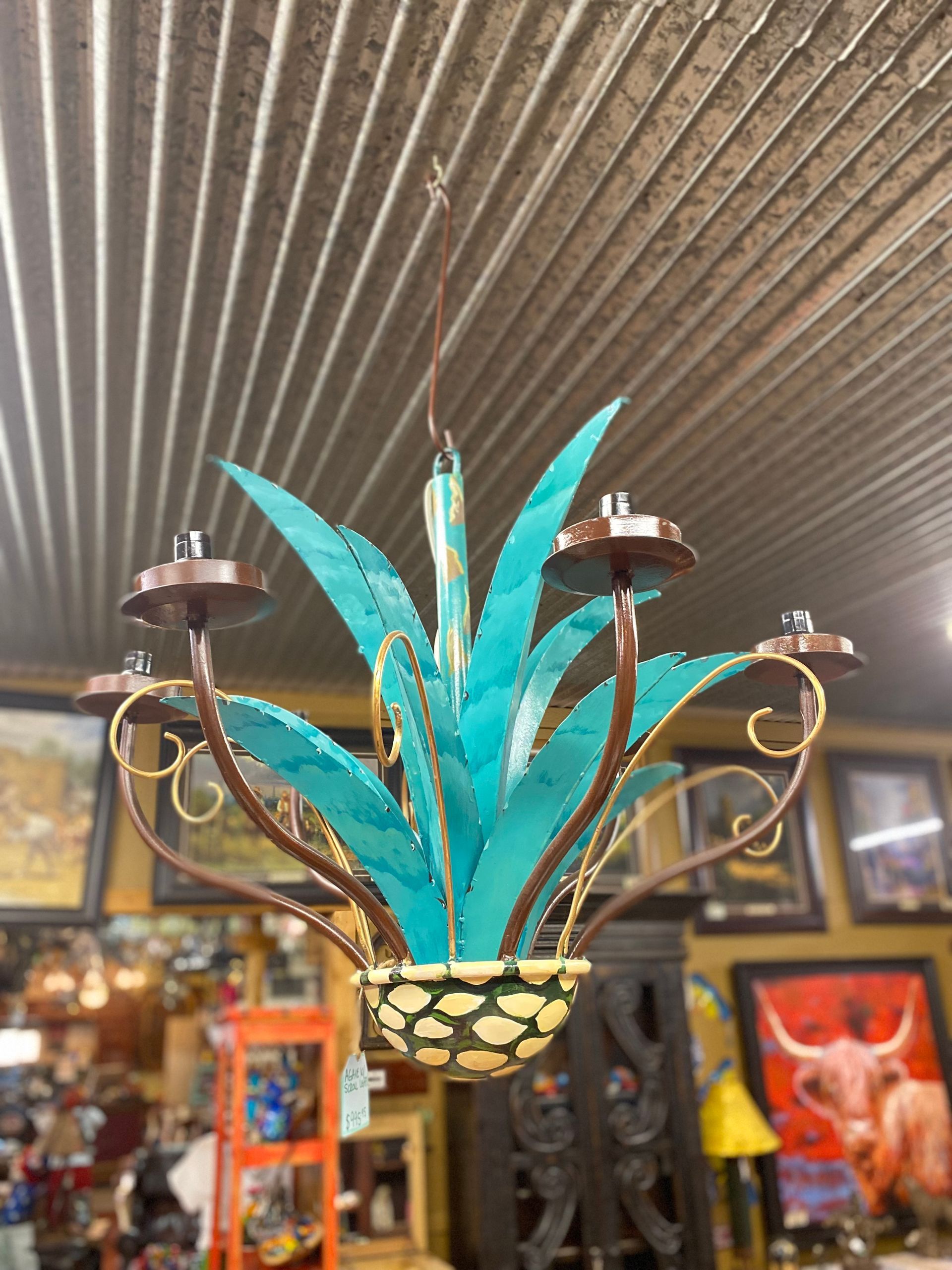 Turquoise metal agave chandelier with brown accents, hanging in a room with artwork on the walls.