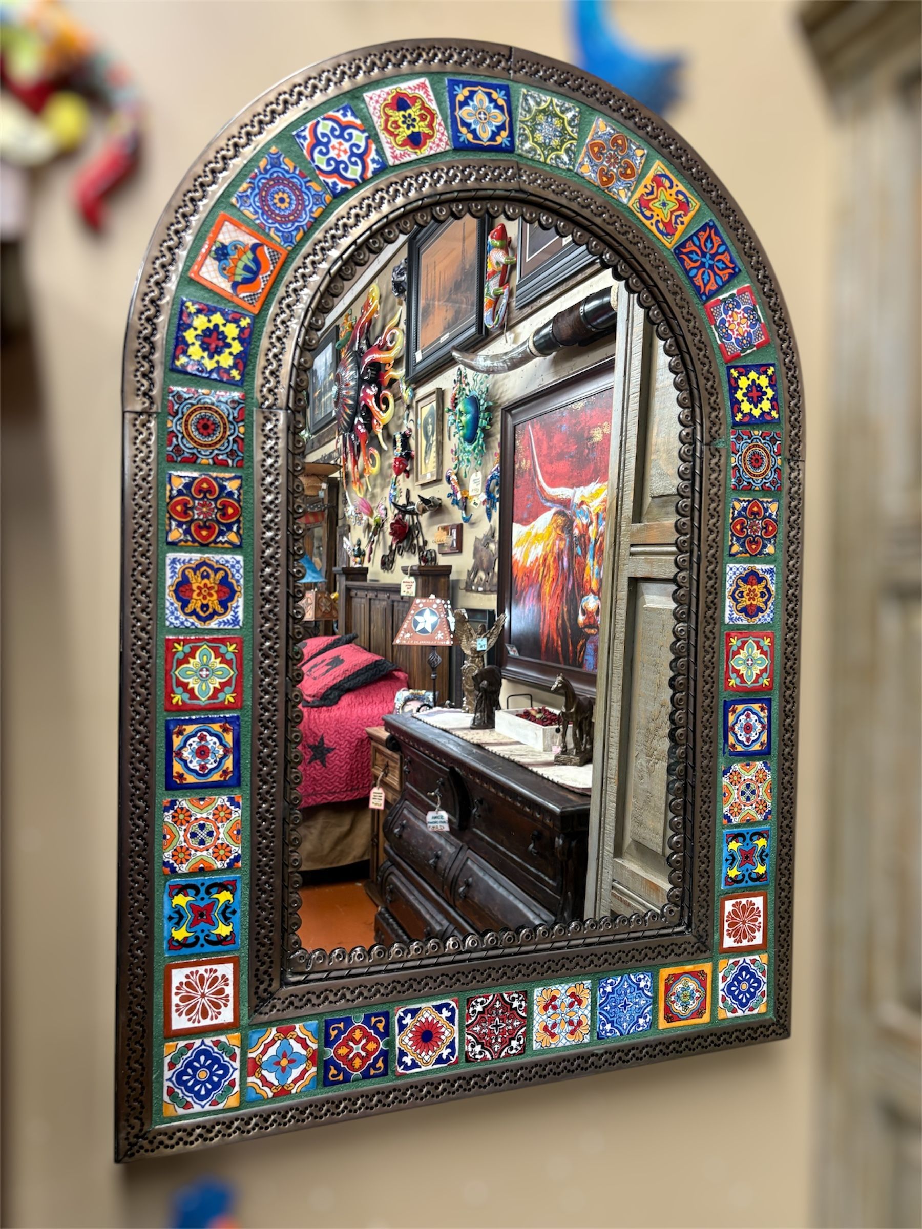 Arched mirror with a mosaic tile border, reflecting a room filled with decorative objects and furniture.